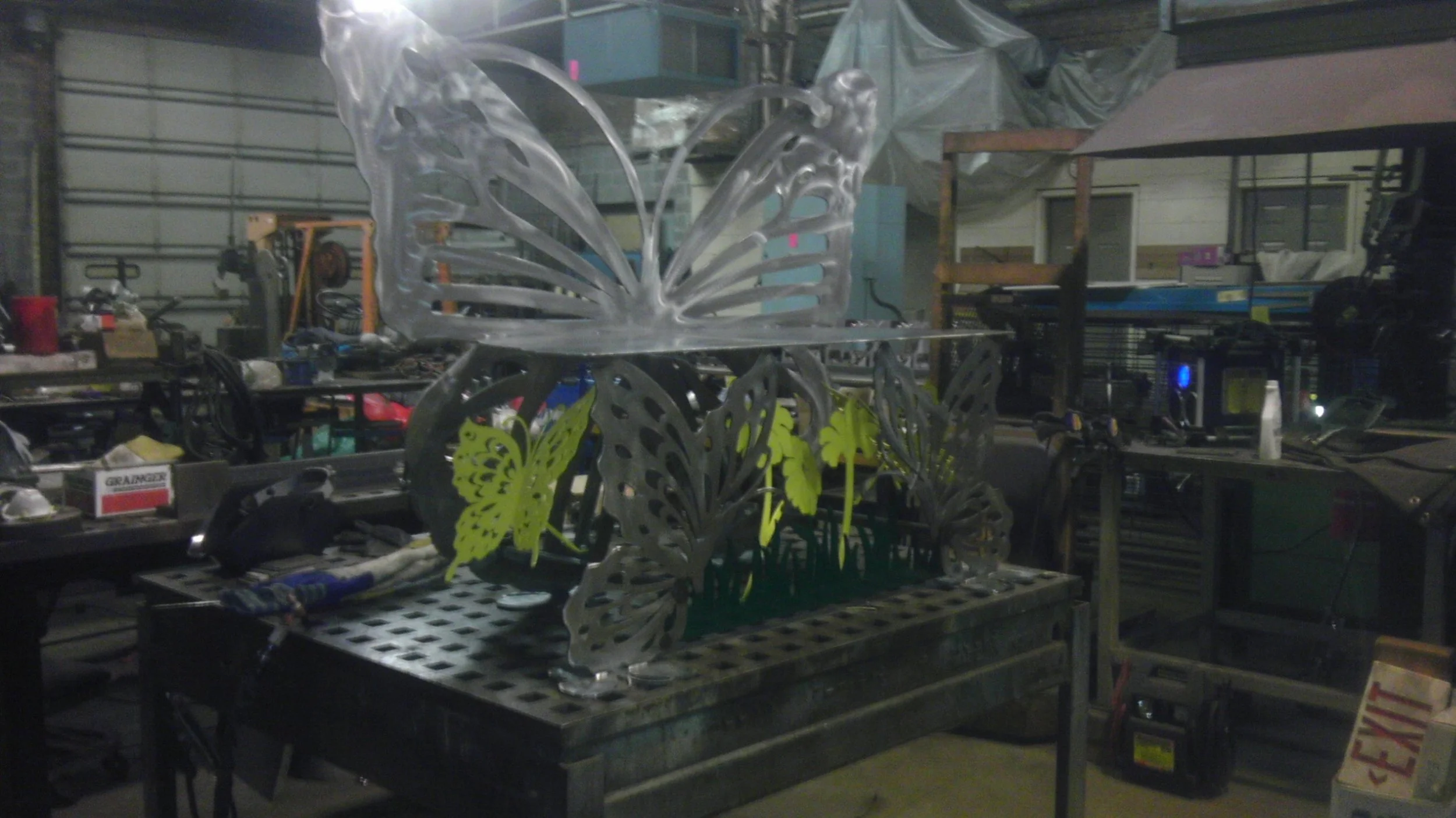 A metal butterfly sculpture with green butterfly accents on a workbench in a workshop.