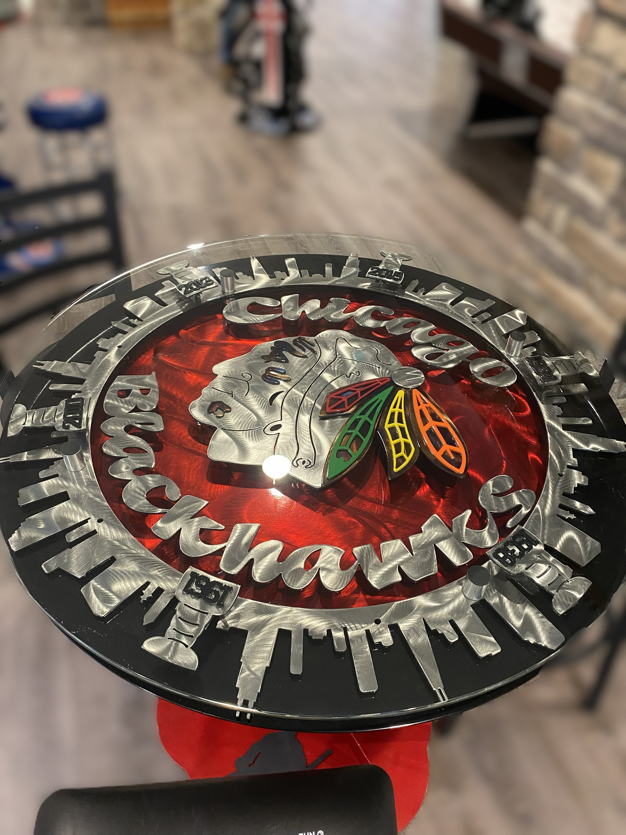 Close-up of a decorative Chicago Blackhawks clock featuring the team logo with a silver Native American head and colorful feathers, against a red background.