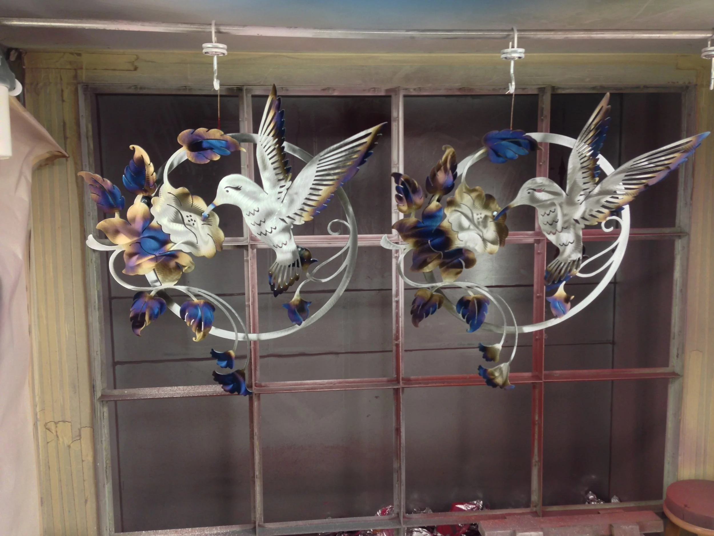 Two decorative wall hangings with white hummingbirds and blue and gold flowers, hanging from the ceiling.