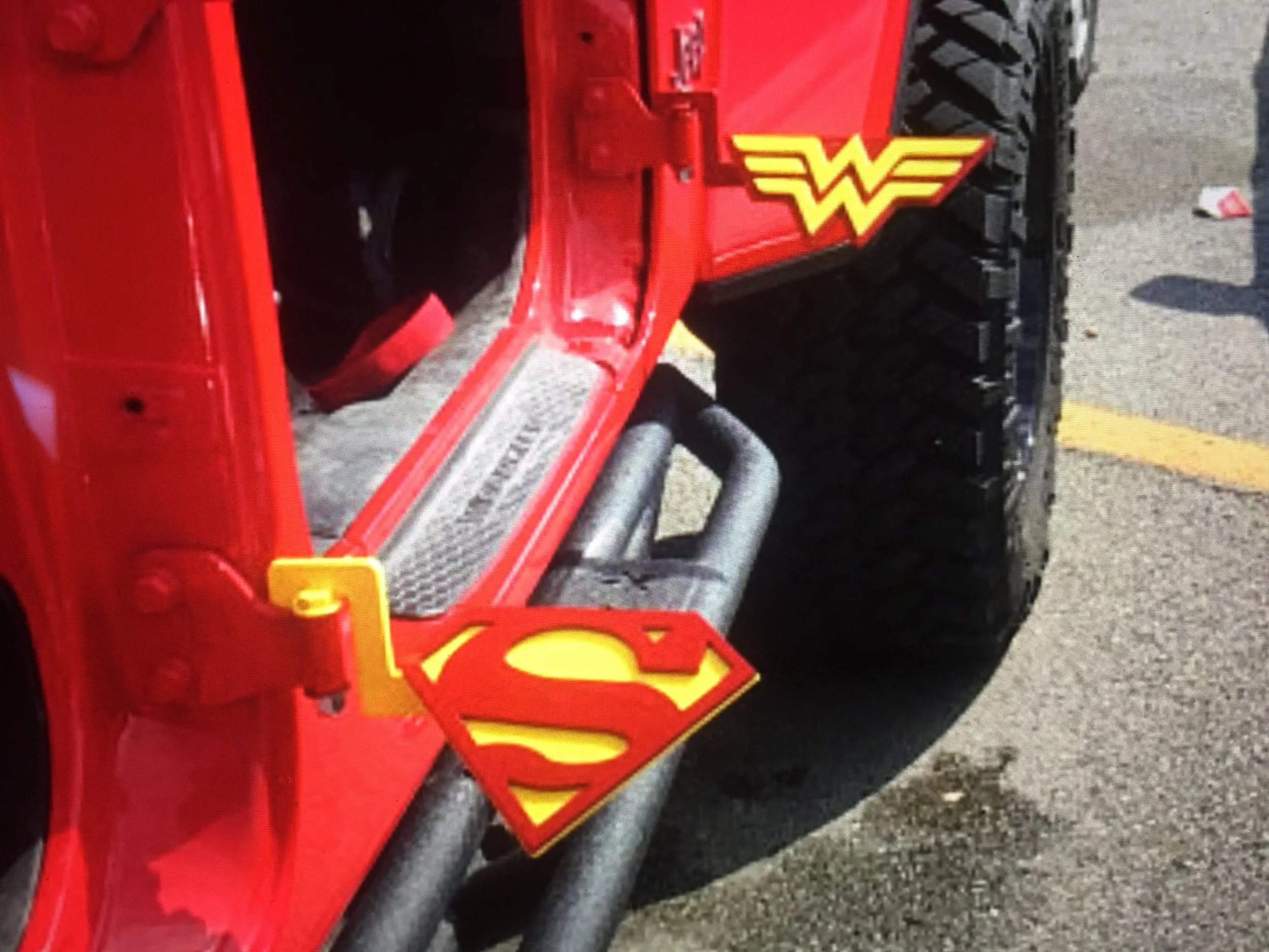 Close-up of a red vehicle with superhero logos, including a Wonder Woman emblem and a Superman emblem, on its side.