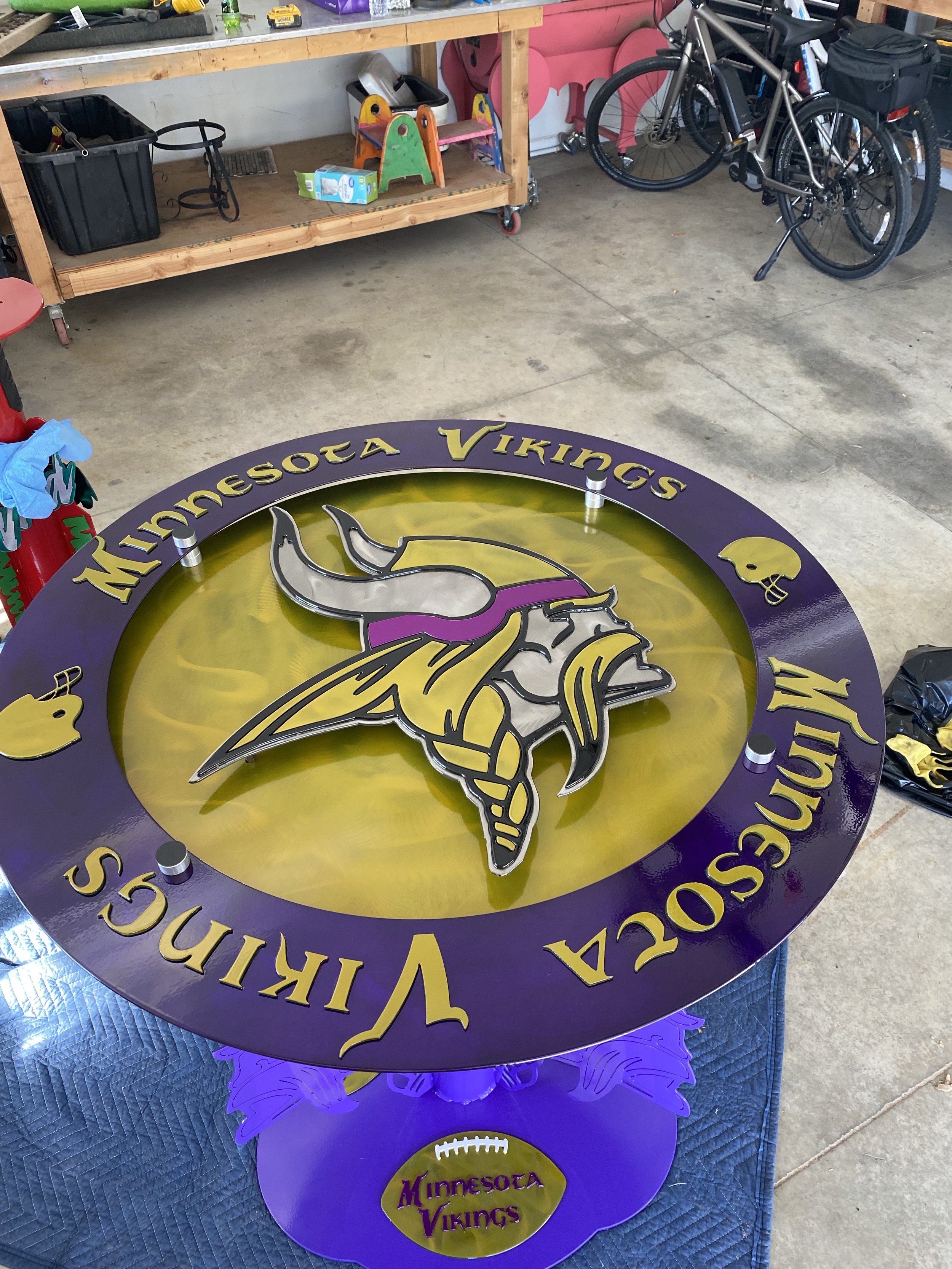 A large circular Minnesota Vikings sign with the team logo of a Viking's head, purple and yellow colors, and the team name around the edge. The sign is on a purple stand.