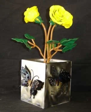 Decorative cube with butterfly images, holding three yellow paper flowers with green leaves and brown stems.