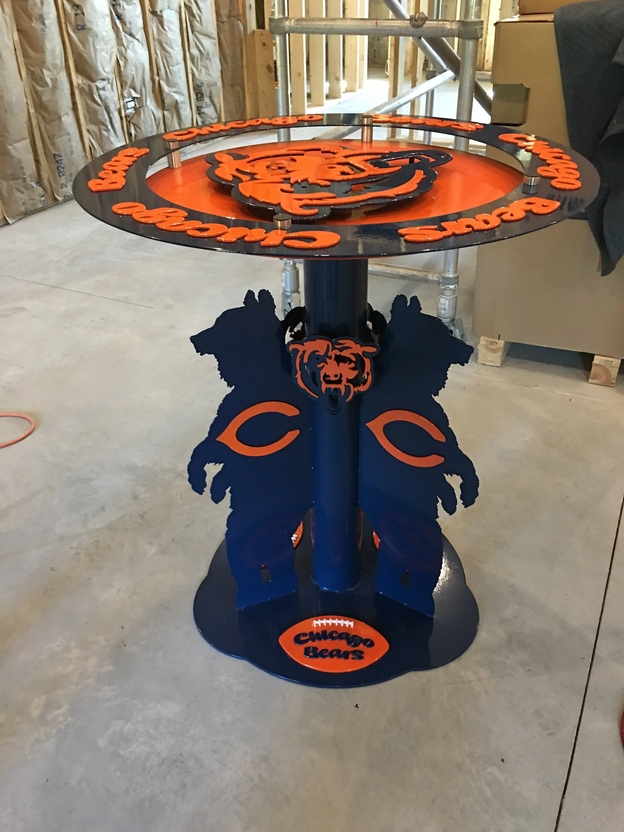 A round table with Chicago Bears logo and branding, featuring a black top with orange accents, and a black base with blue and orange bear head designs.