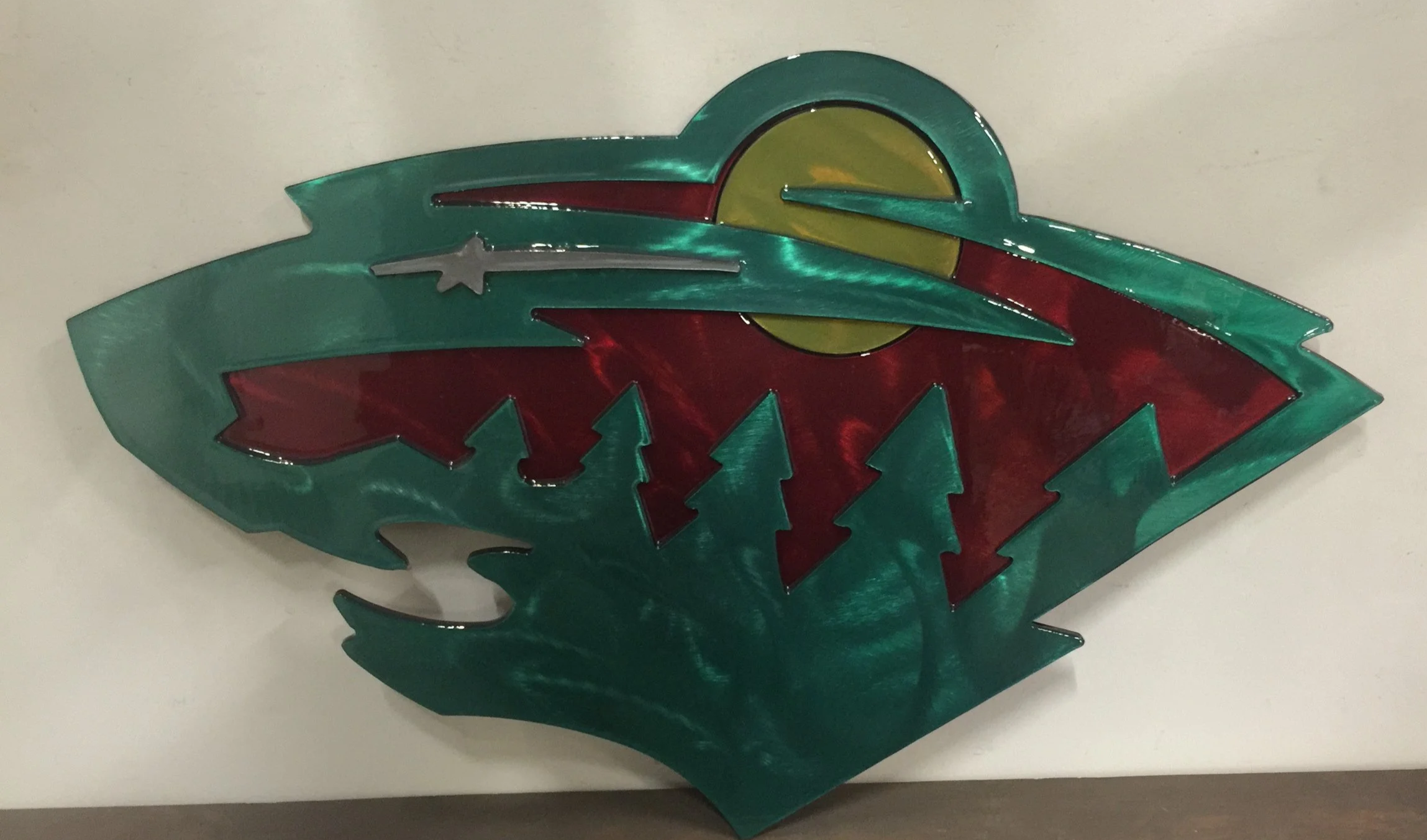 A decorative art piece resembling a landscape with a large green mountain, red trees, a green horizon, and a yellow sun or moon in a stylized, abstract design.
