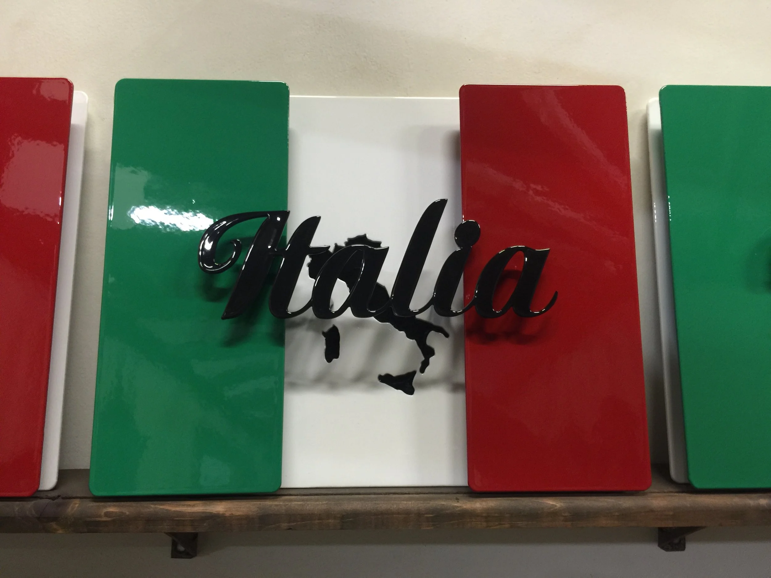 Decorative sign with the word 'Italia' in black cursive letters and an outline of Italy, on a background with vertical red, white, and green stripes.