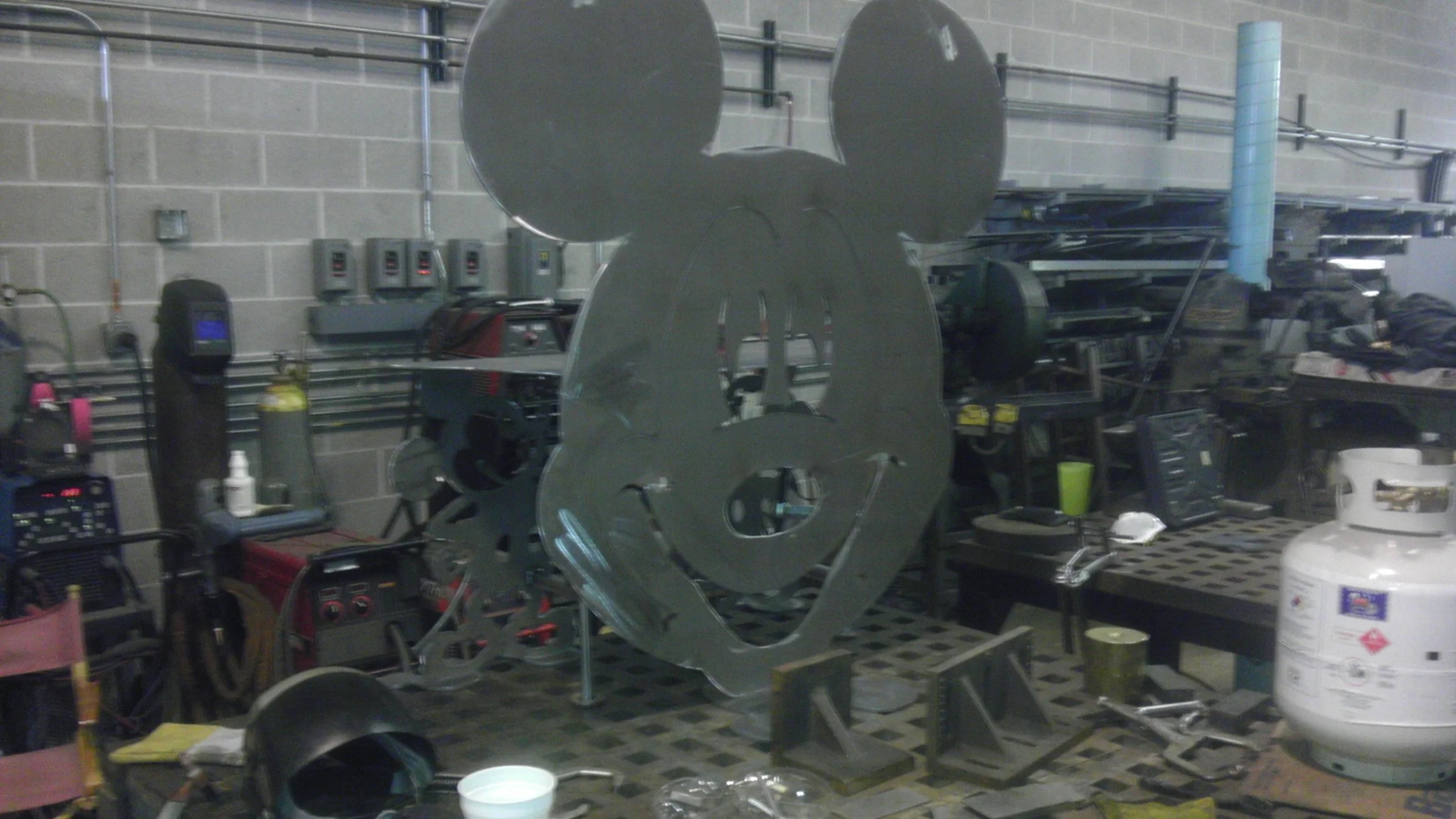 Metal sculpture of Mickey Mouse's head on a workbench in a workshop.