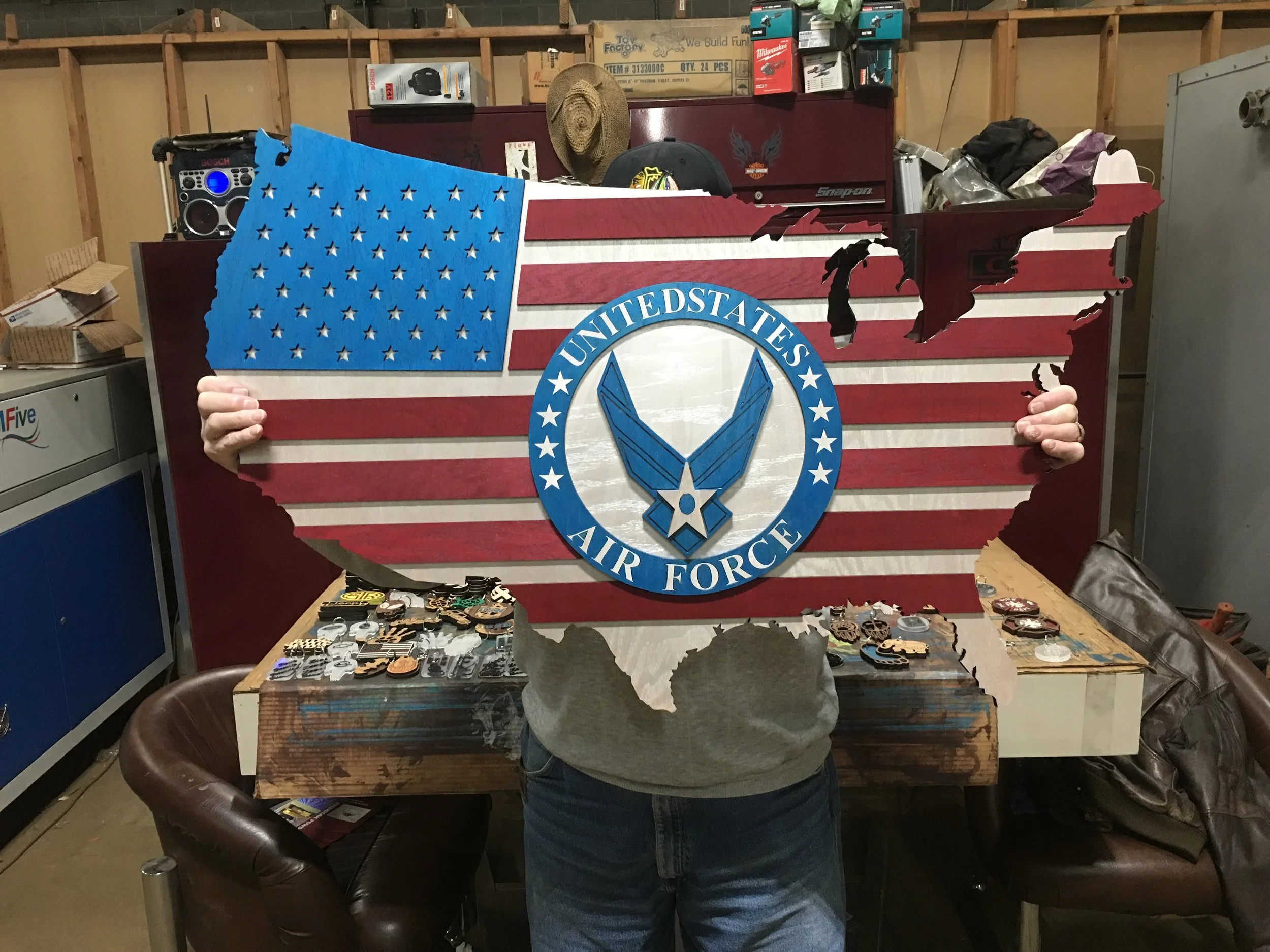 A person holding a large wooden US flag with a United States Air Force emblem in the center.