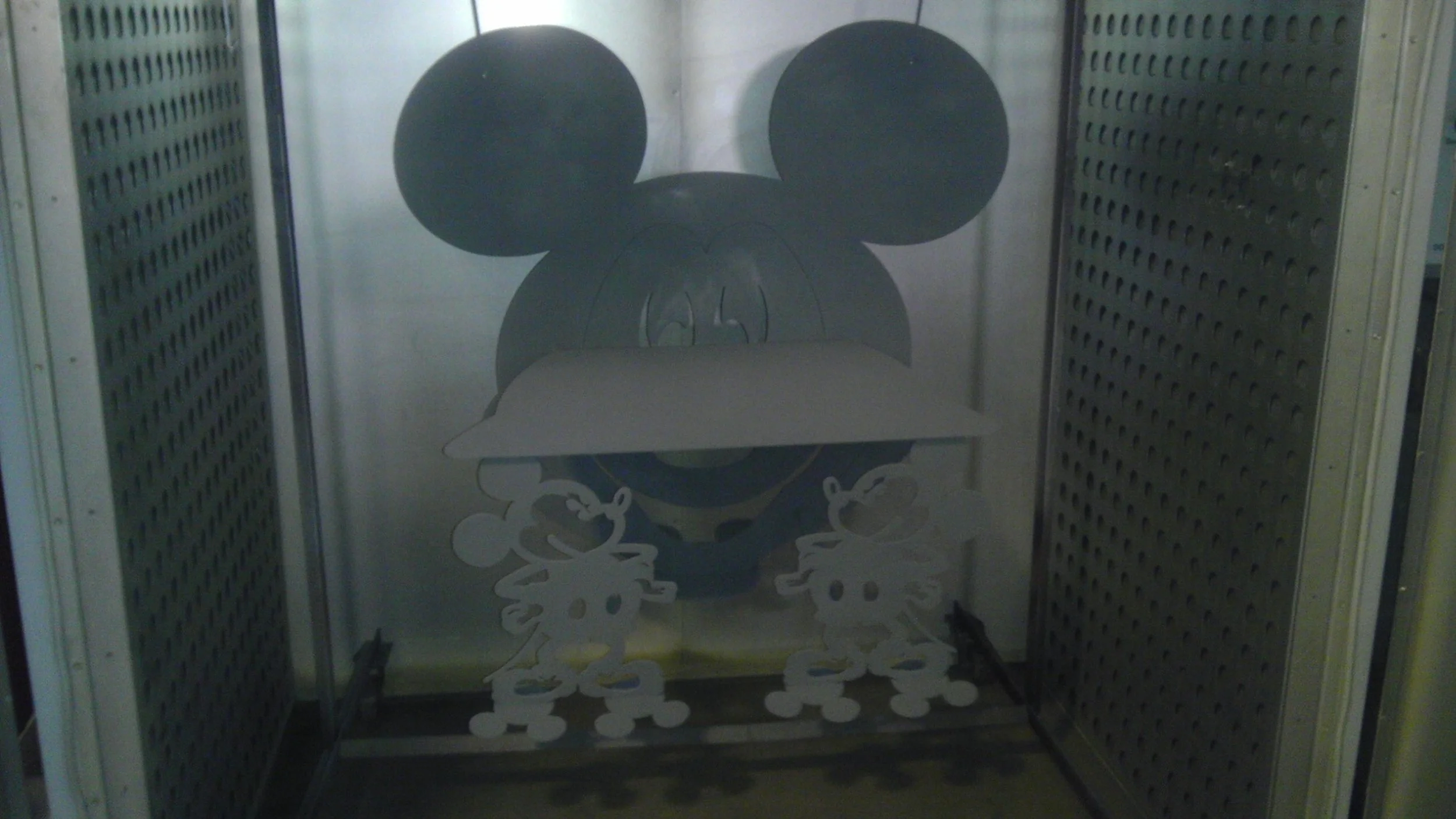 A decorative sticker of Mickey Mouse wearing a cowboy hat, with two smaller mice characters, on a glass door or window with metal panels on each side.