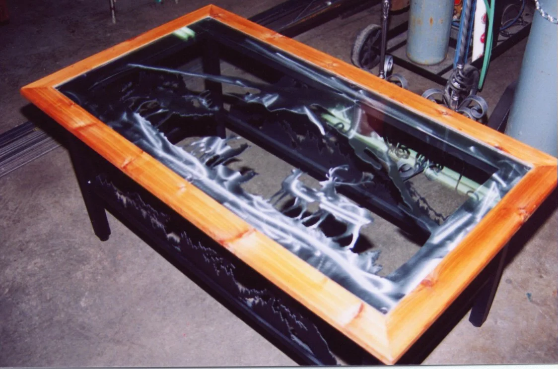 A wooden-framed glass tabletop with a black surface, placed on a worktable in a workshop setting.
