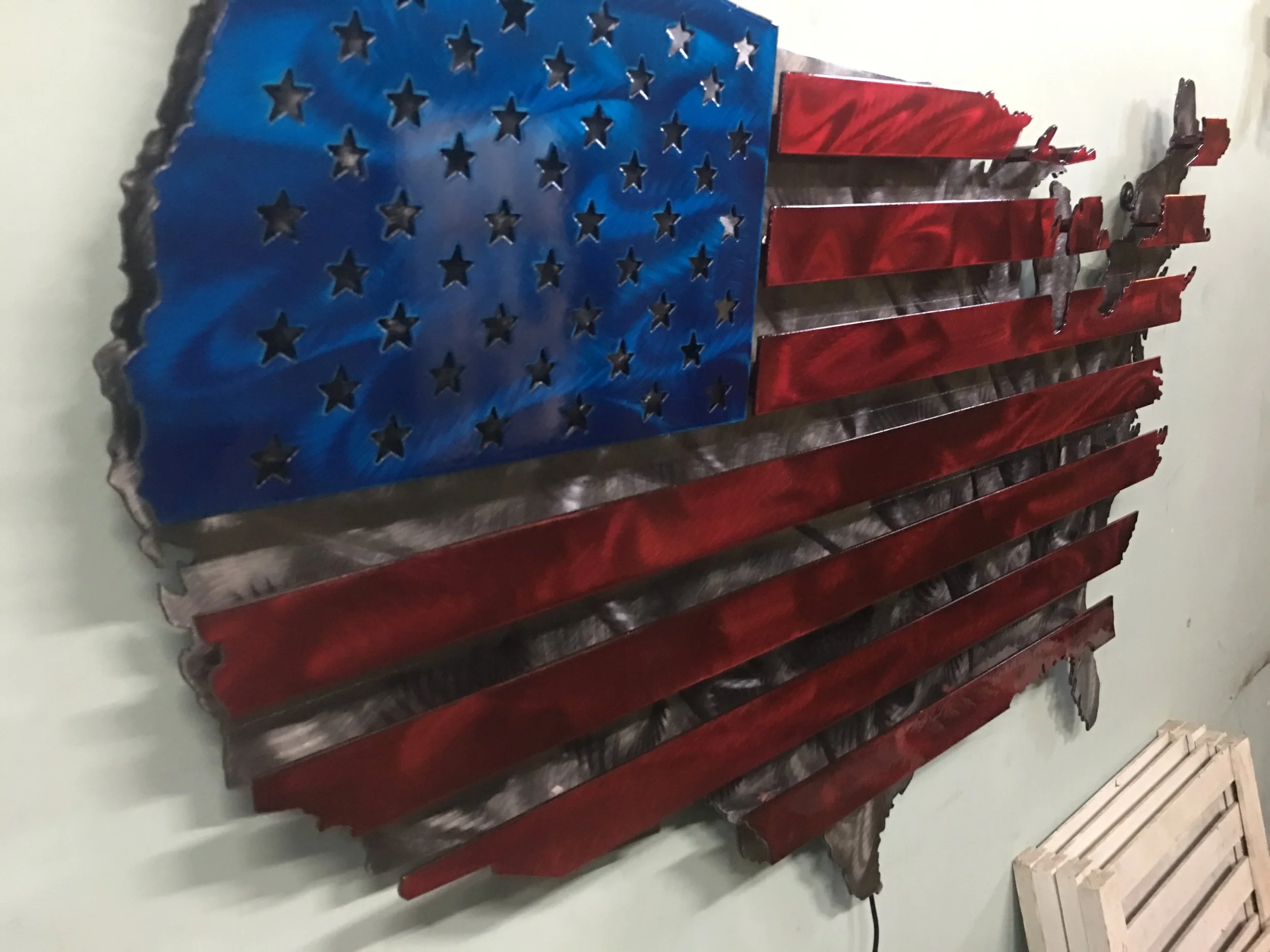 Wall-mounted metal American flag with stars on a blue field and red and silver stripes.