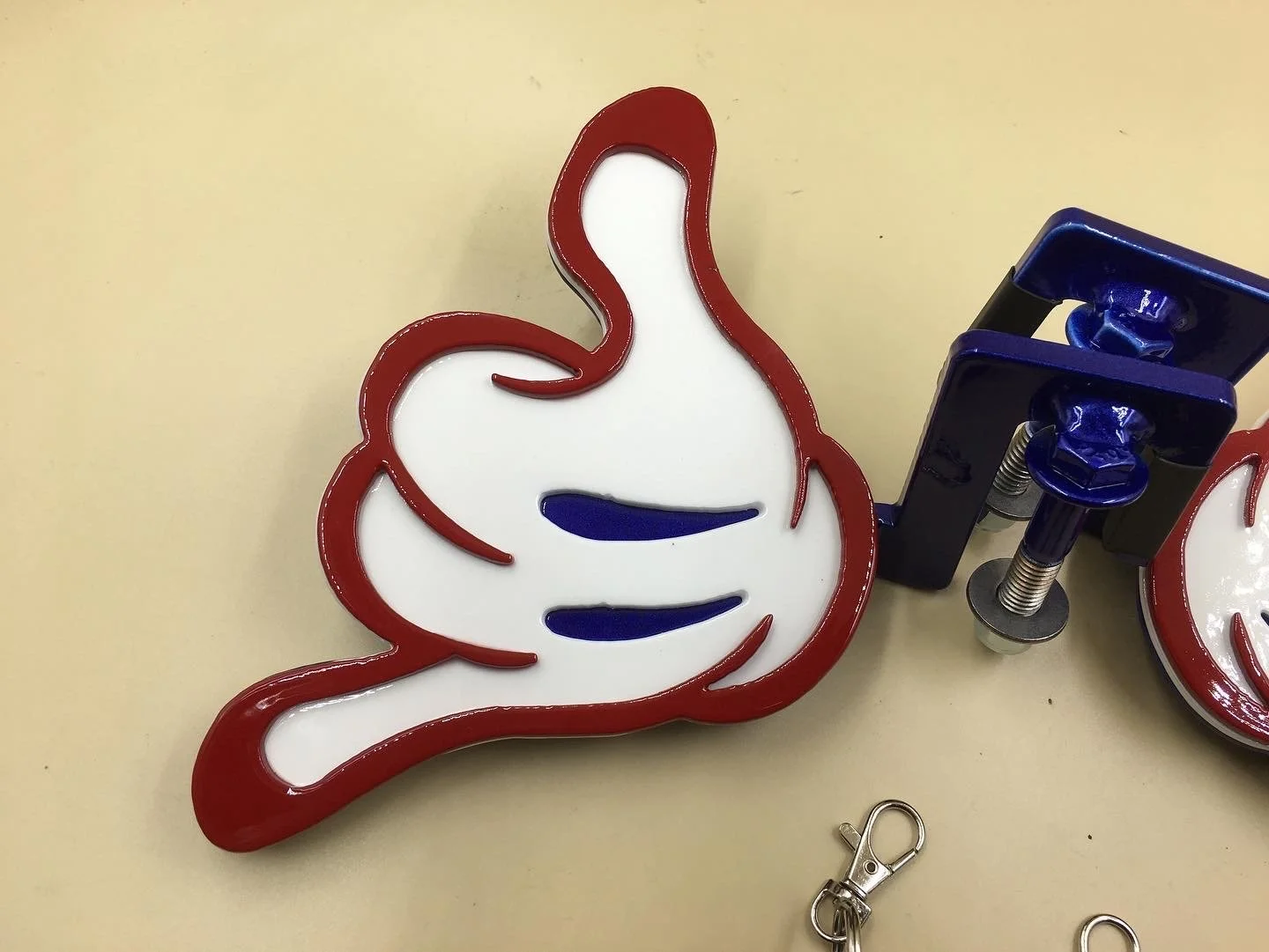 Neon sign of a thumbs-up with red outline, white inside, and blue accents, mounted on a beige wall.
