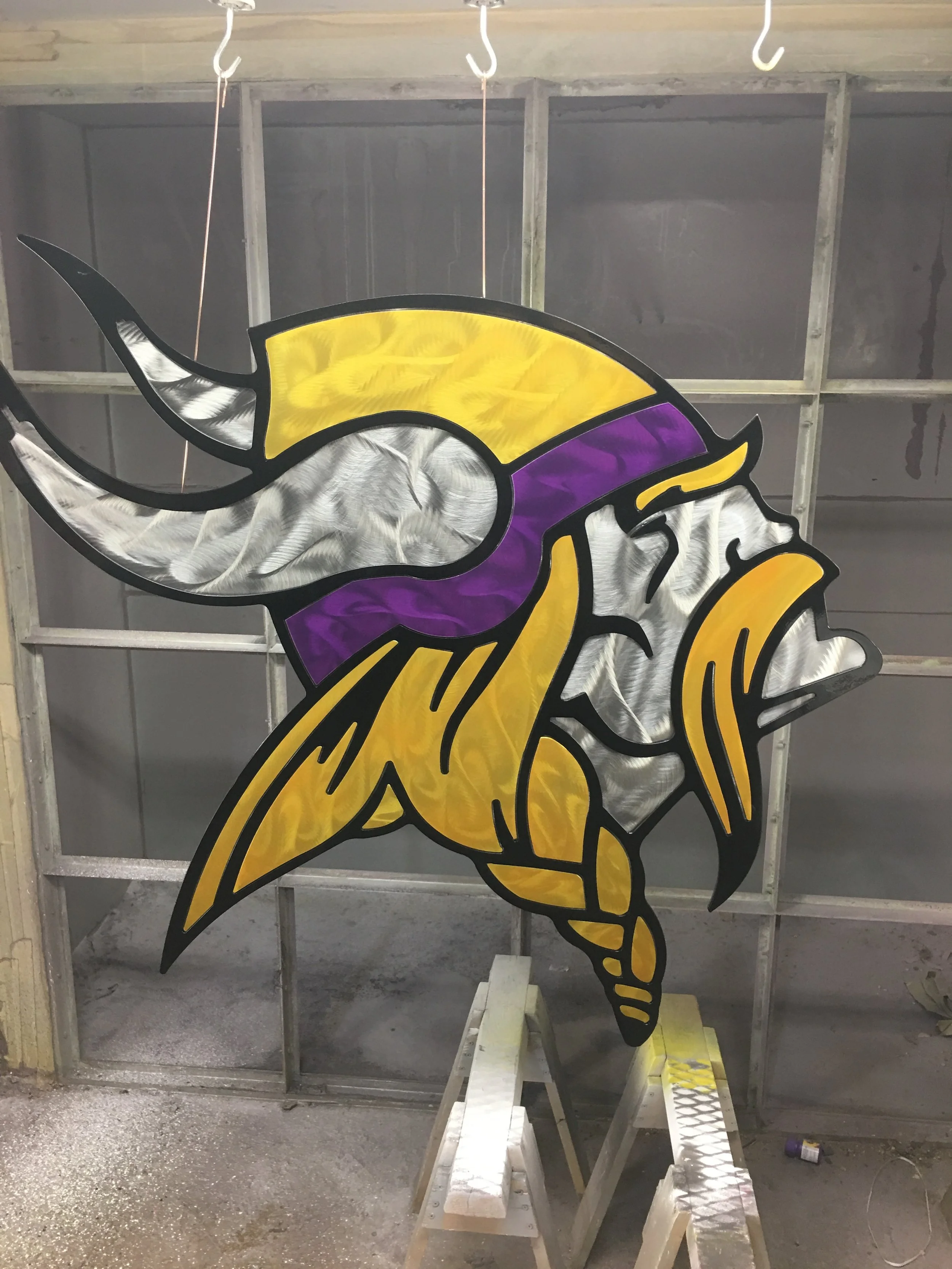 Stained glass artwork of a Vikings football helmet with purple, yellow, silver, and black colors, placed on a stand in a workshop.