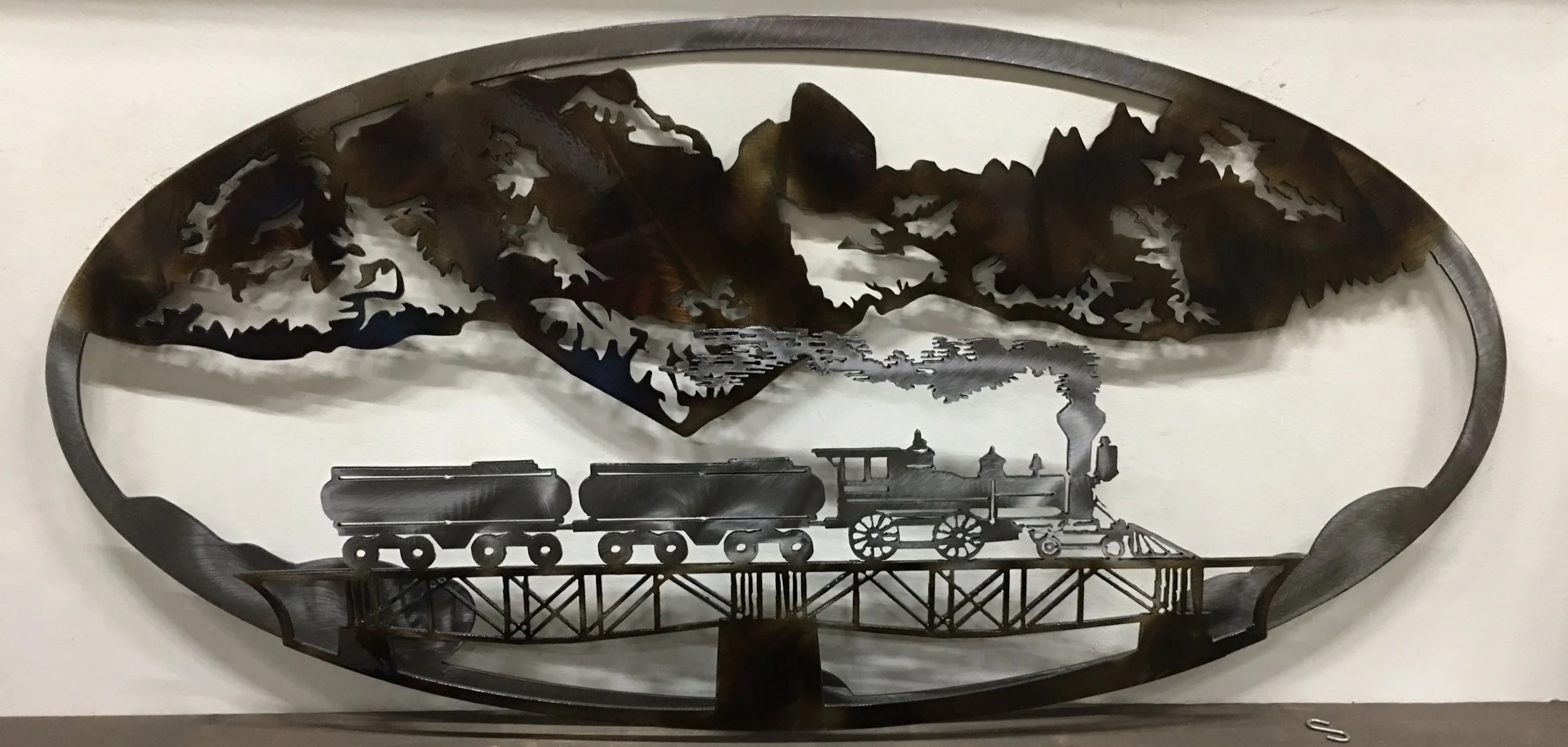 Metal wall art depicting a steam train crossing a bridge with mountain scenery in the background.