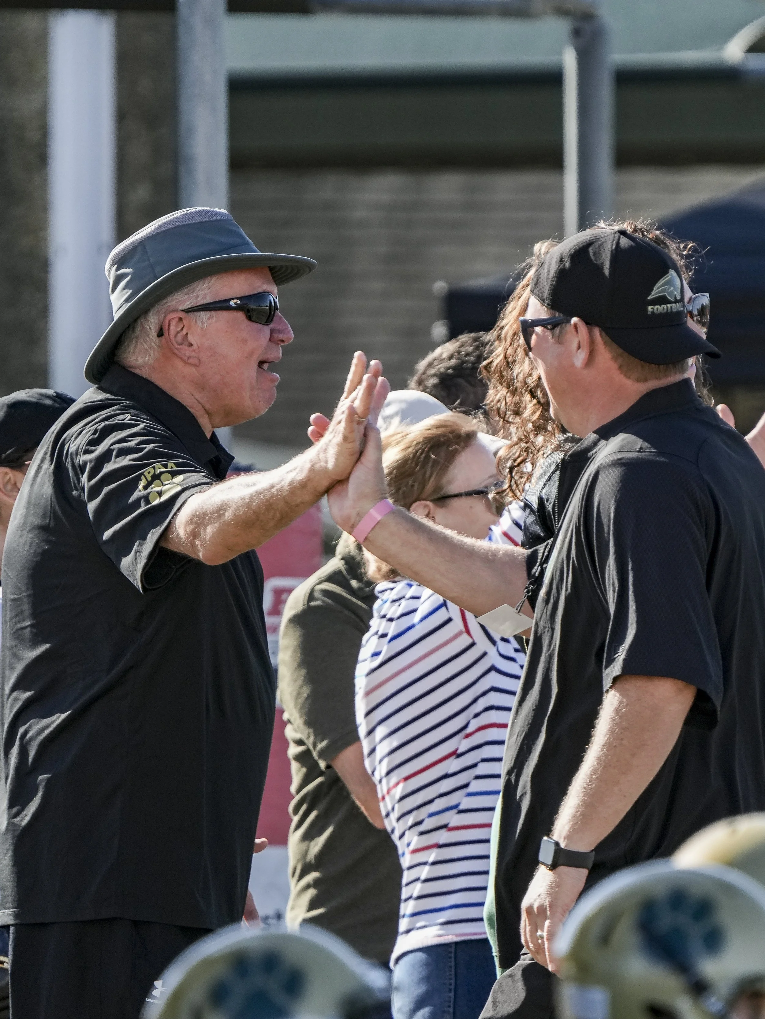 Two men giving each other a high five during a sports event, with a crowd of spectators in the background.