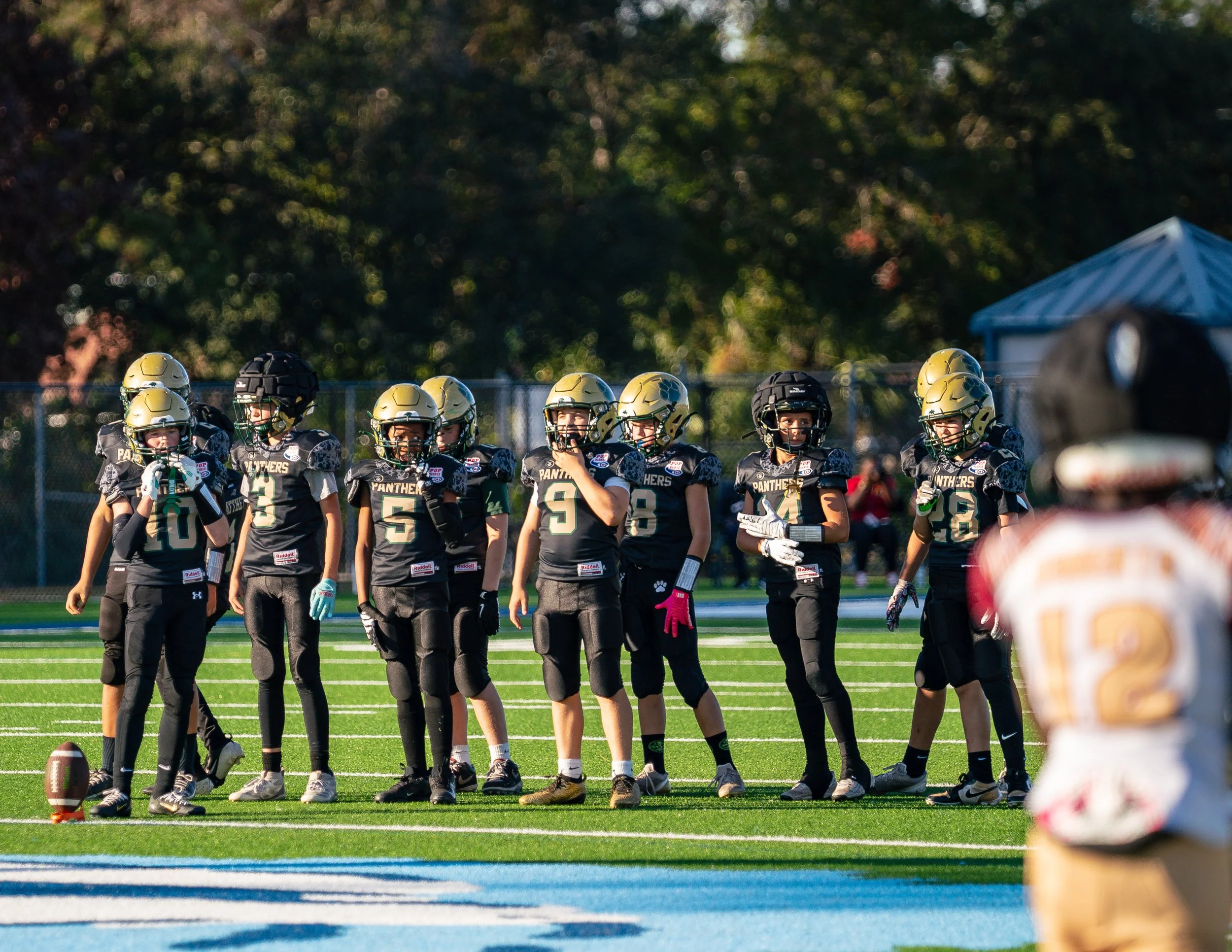 Youth football team in black uniforms with gold helmets standing on a football field during a game or practice.