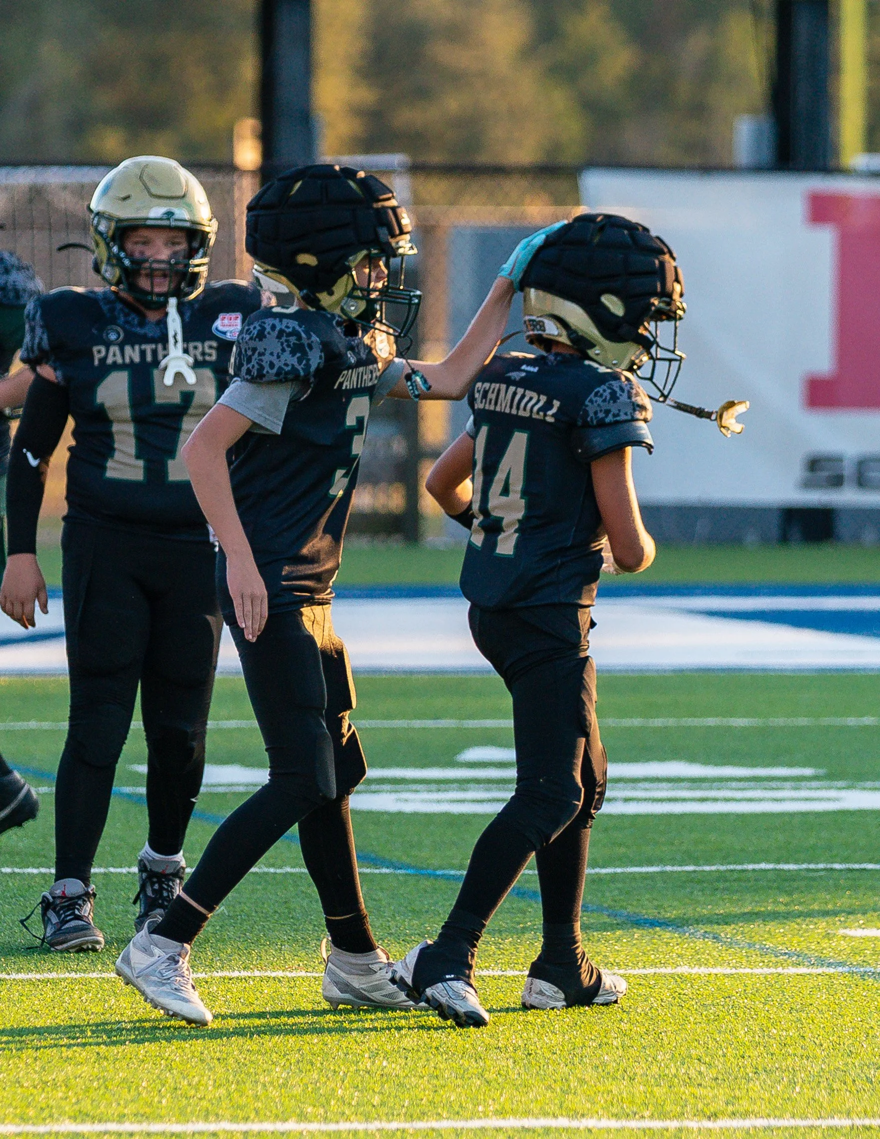 Youth football players in black and gold uniforms on a football field, celebrating during a game.