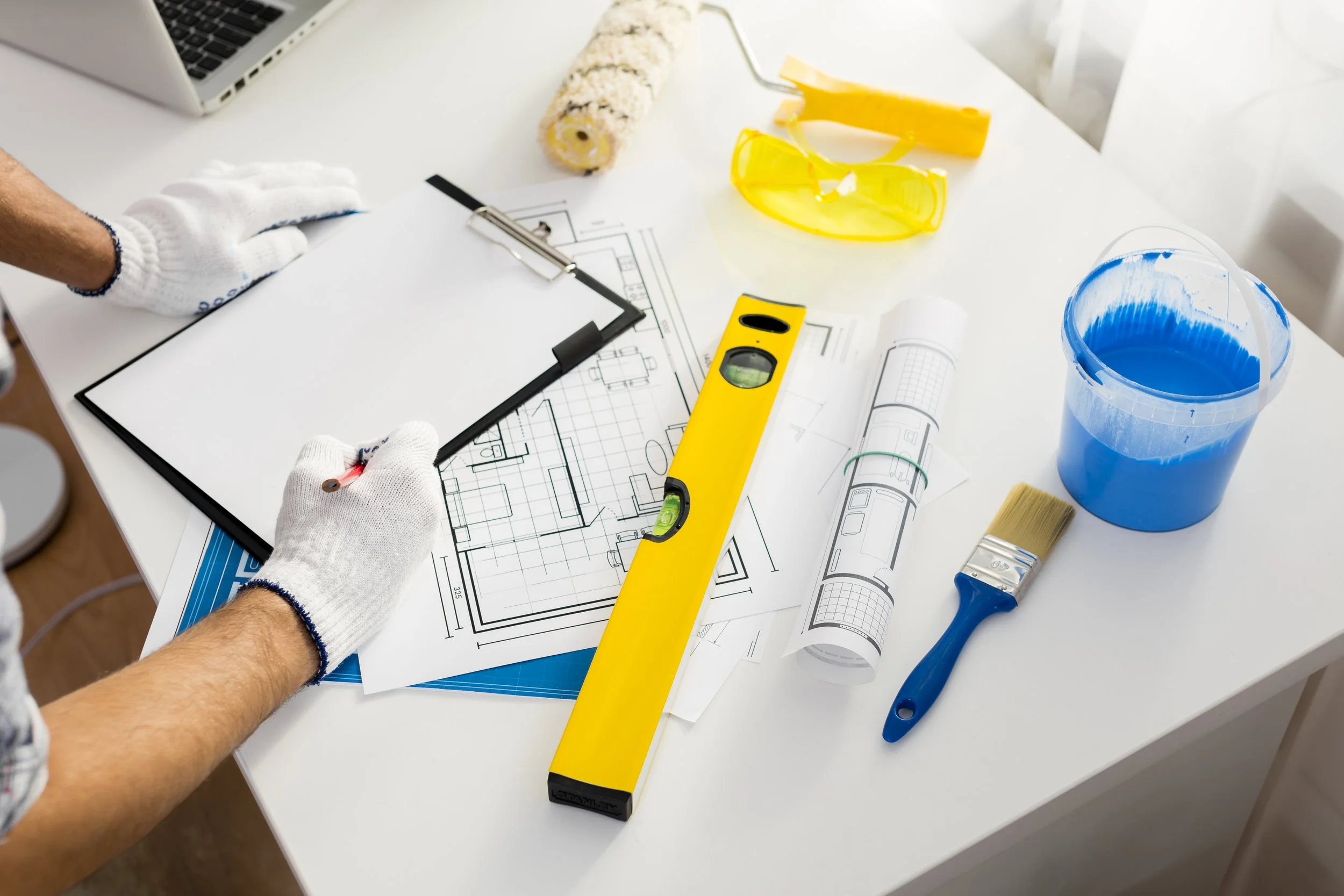 Architect working on building plans with tools and paint supplies on a white table