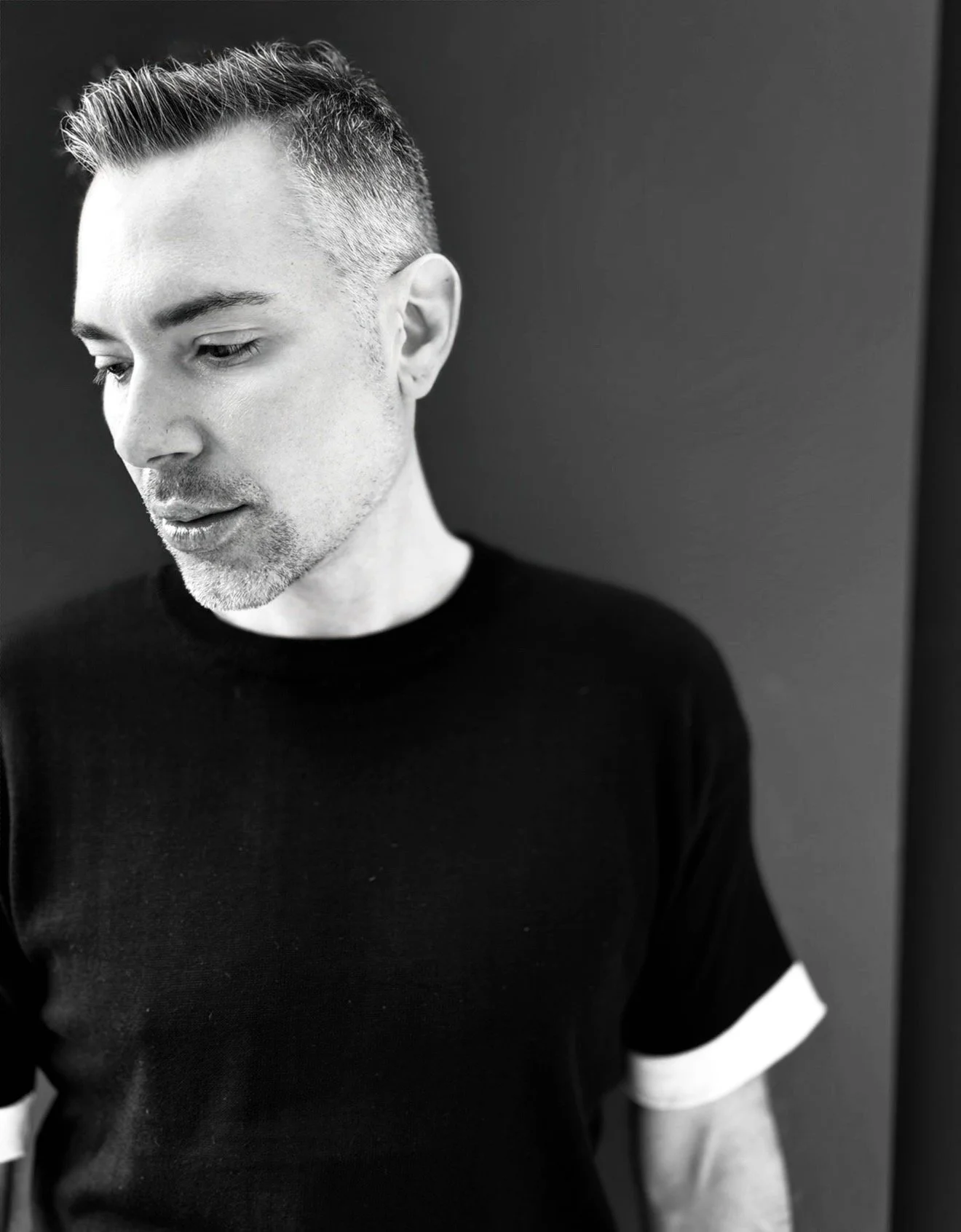 A black-and-white photo of a founder, Brice Terrible,  with short, styled hair and a trimmed beard, looking down and to his left, wearing a black shirt with white trim on the sleeves.