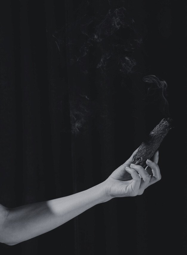 A black and white photo of a hand holding a piece of burning natural ingredients.