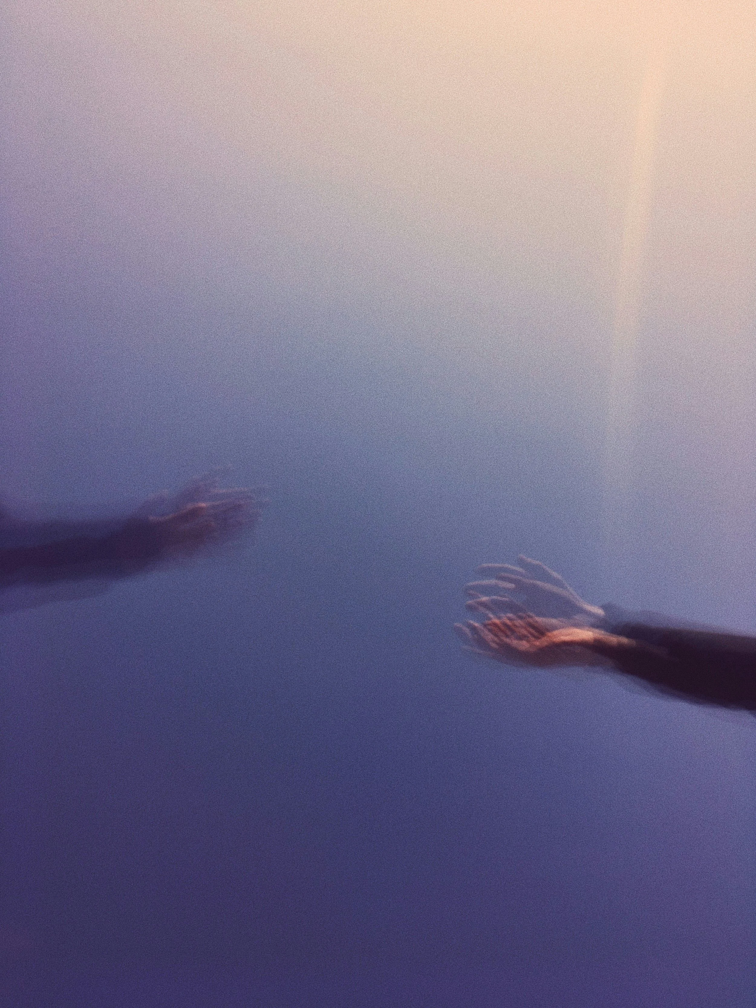 Multiple hands reaching upward in a sky with a rainbow.