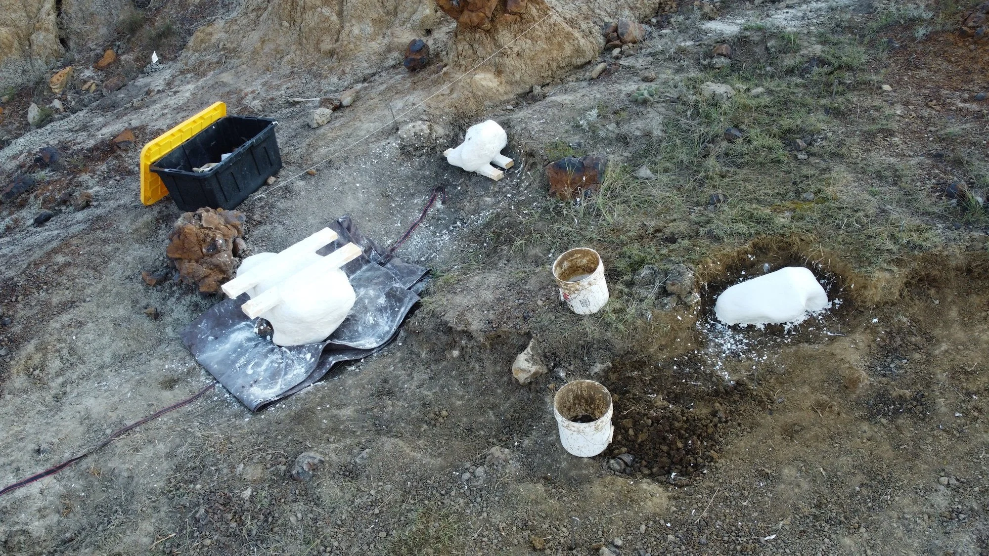 Excavation site with buckets, foam molds, and work tools, likely for archaeological or construction purposes.