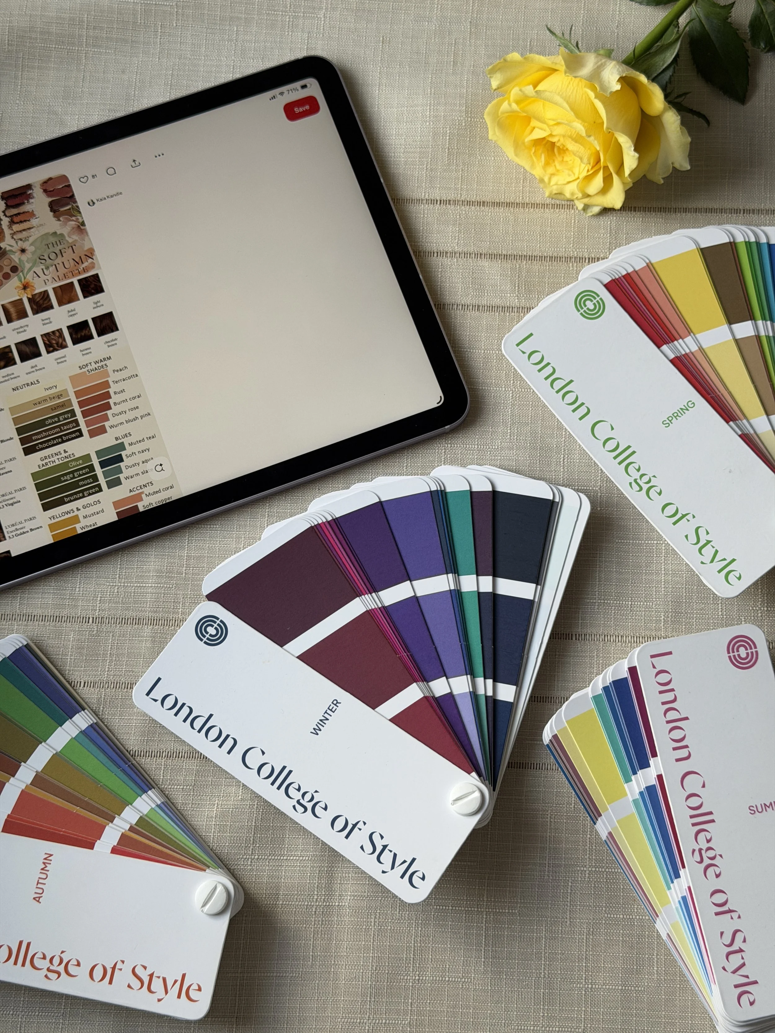 Color swatch cards labeled 'London College of Style' in different seasonal collections, a tablet with a color palette on the screen, and a yellow rose on a beige tablecloth.