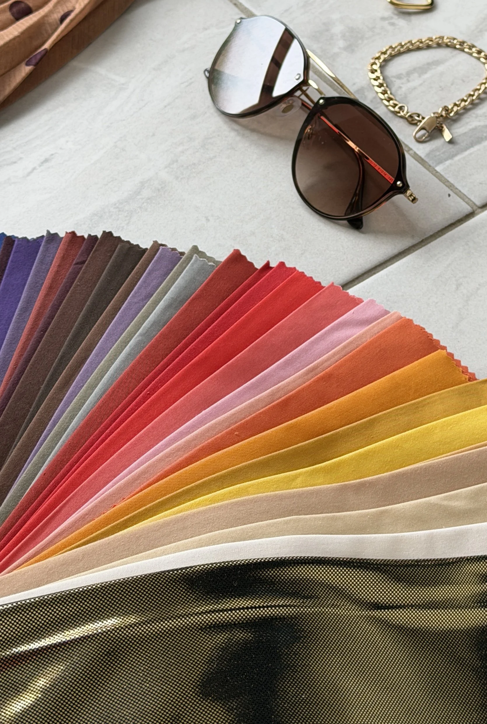 Color swatches, sunglasses, gold bracelet, and jewelry on a white surface.