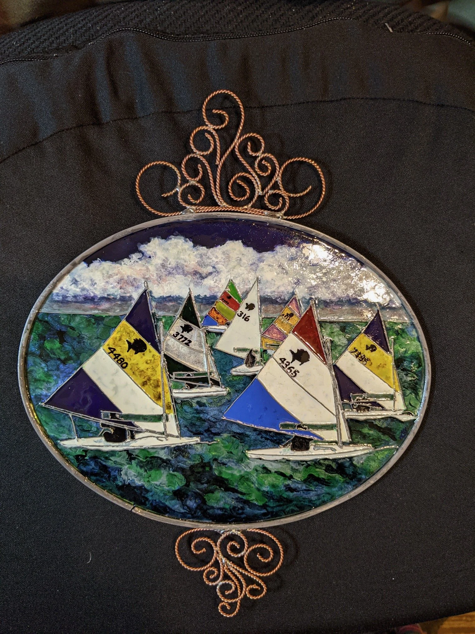 Sunfish Regatta by Art Illusions by Young photographed against a black background and prior to the addition of beadwork. The colorful sailboats race across the water with high contrast, highlighting the hand-painted sails and copper wire framing. Thi
