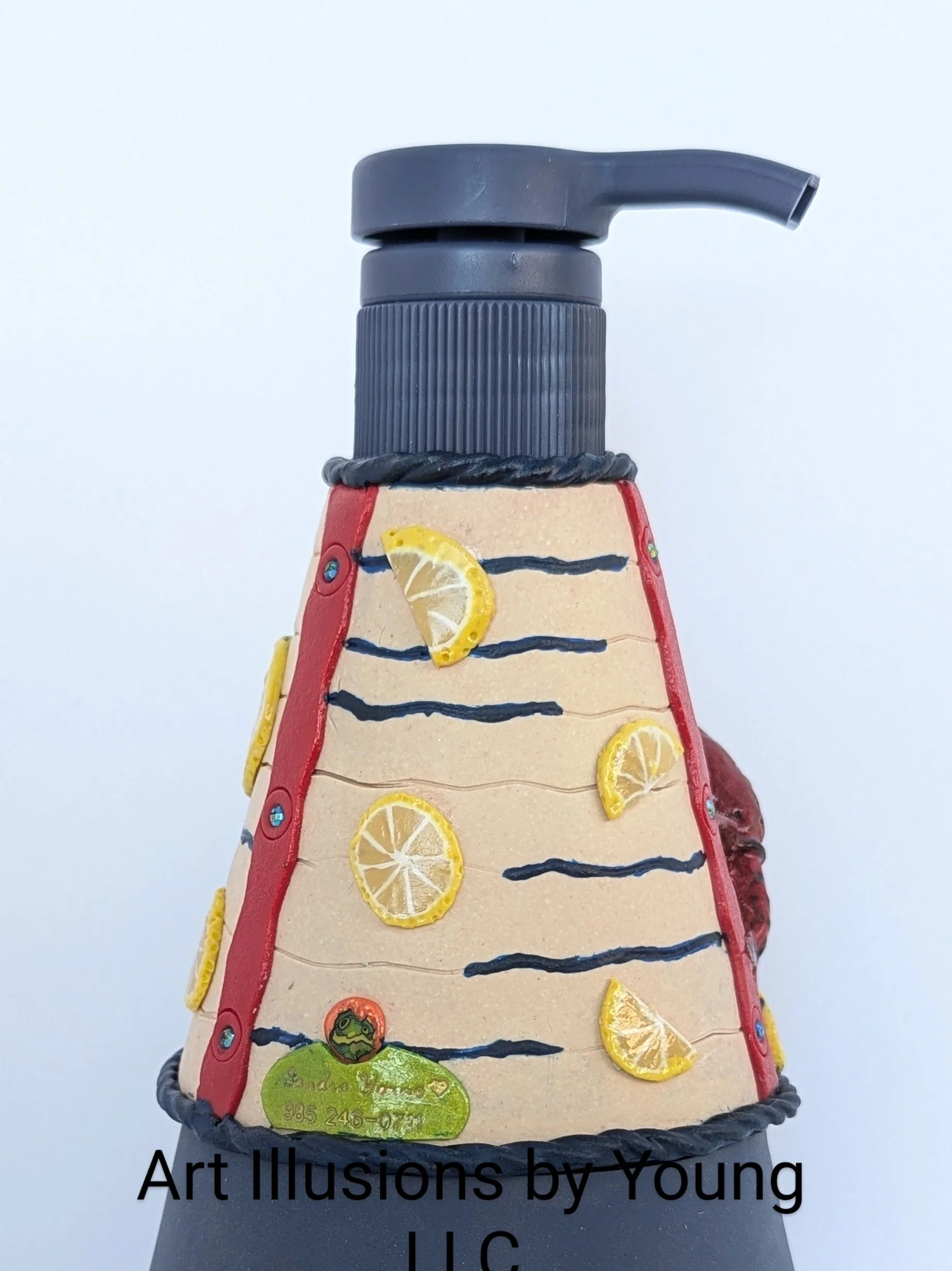 Side profile of the Crawfish Boil Soap Dispenser by Art Illusions by Young. The navy pump dispenser rises above the richly textured polymer clay surface, where hand-sculpted crawfish, corn, and lemon slices rest on a neutral “newsprint” background. L