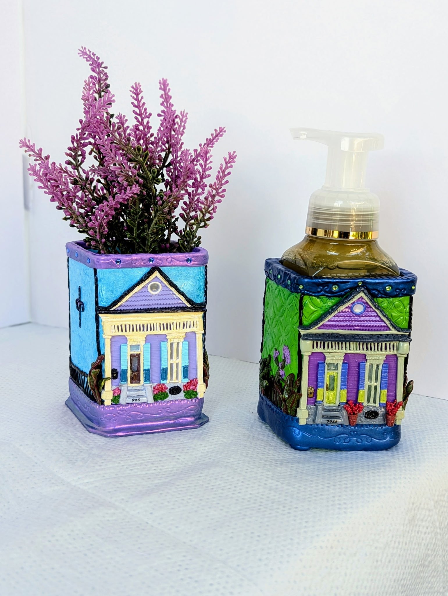 🟢 Available :
These handcrafted functional art pieces capture the vibrant charm of historic Creole shotgun houses. One features a soft lavender facade with blue shutters and ornate gingerbread trim; the other displays a rich purple exterior accented