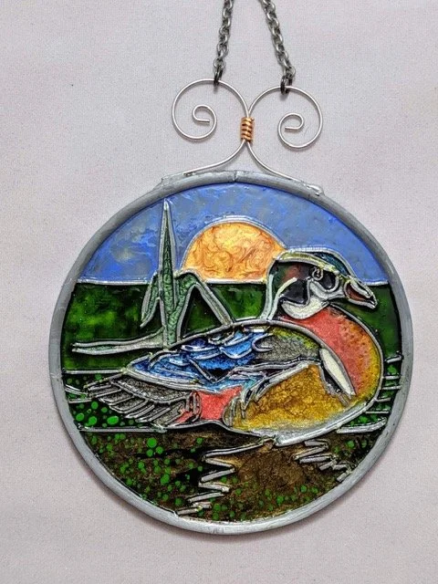 🔴 Sold: 
Wood Duck Illusion Glass by Art Illusions by Young. A graceful wood duck glides across calm water in this serene circular suncatcher, surrounded by cattails and reeds. Rich earth tones and subtle reflections in European glass paints capture