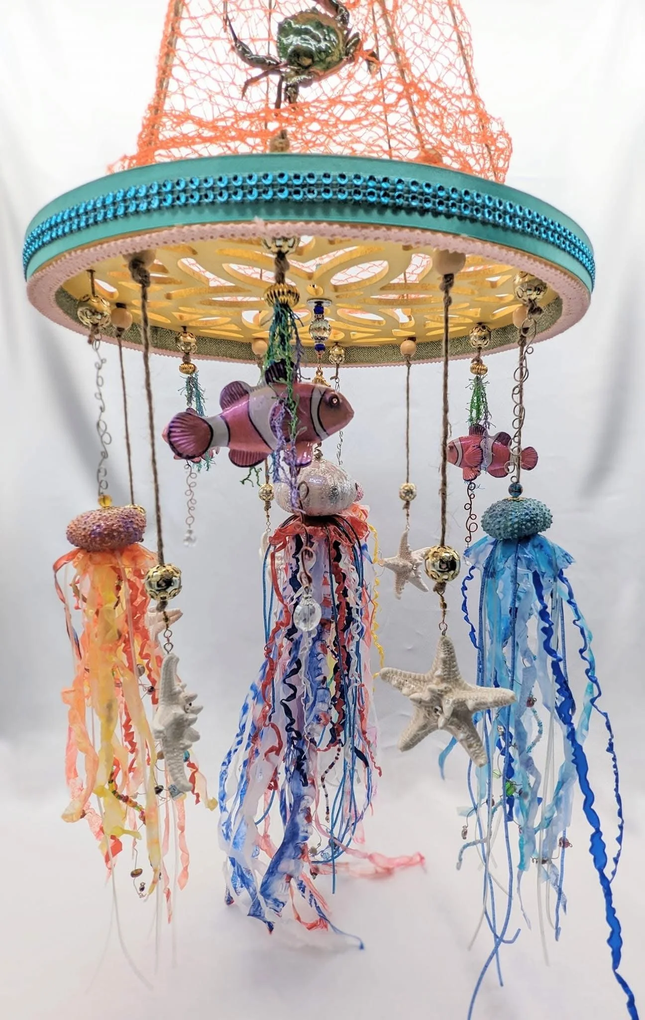 Close-up of the Nautical Jellyfish Mobile by Art Illusions by Young. The scrollwork wooden hanger supports a decorative netted canopy beneath which four handcrafted sea urchin jellyfish with flowing tentacles and iridescent details gently drift. Embe