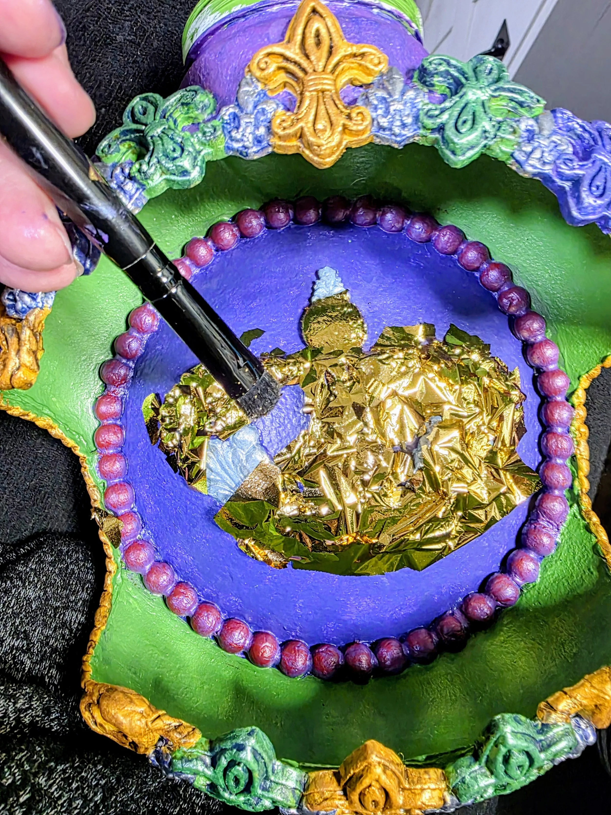 Dual Crown Royalty Ornament – Gold Leaf Application
This regal Dual Crown Royalty Ornament is shown in its final stages of creation. Intricate polymer clay details form two elegant crowns, now receiving a luxurious application of shimmering gold leaf