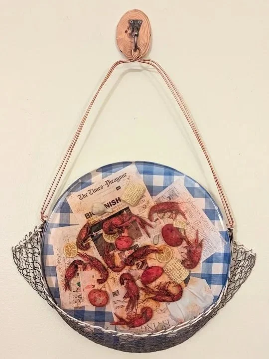 Crawfish Boil Epoxy Wall Art by Art Illusions by Young from Folsom, Louisiana. The completed mixed-media masterpiece is displayed hanging in a decorative woven crab net and set onto a blue gingham tablecloth. Hand-sculpted polymer clay crawfish, corn