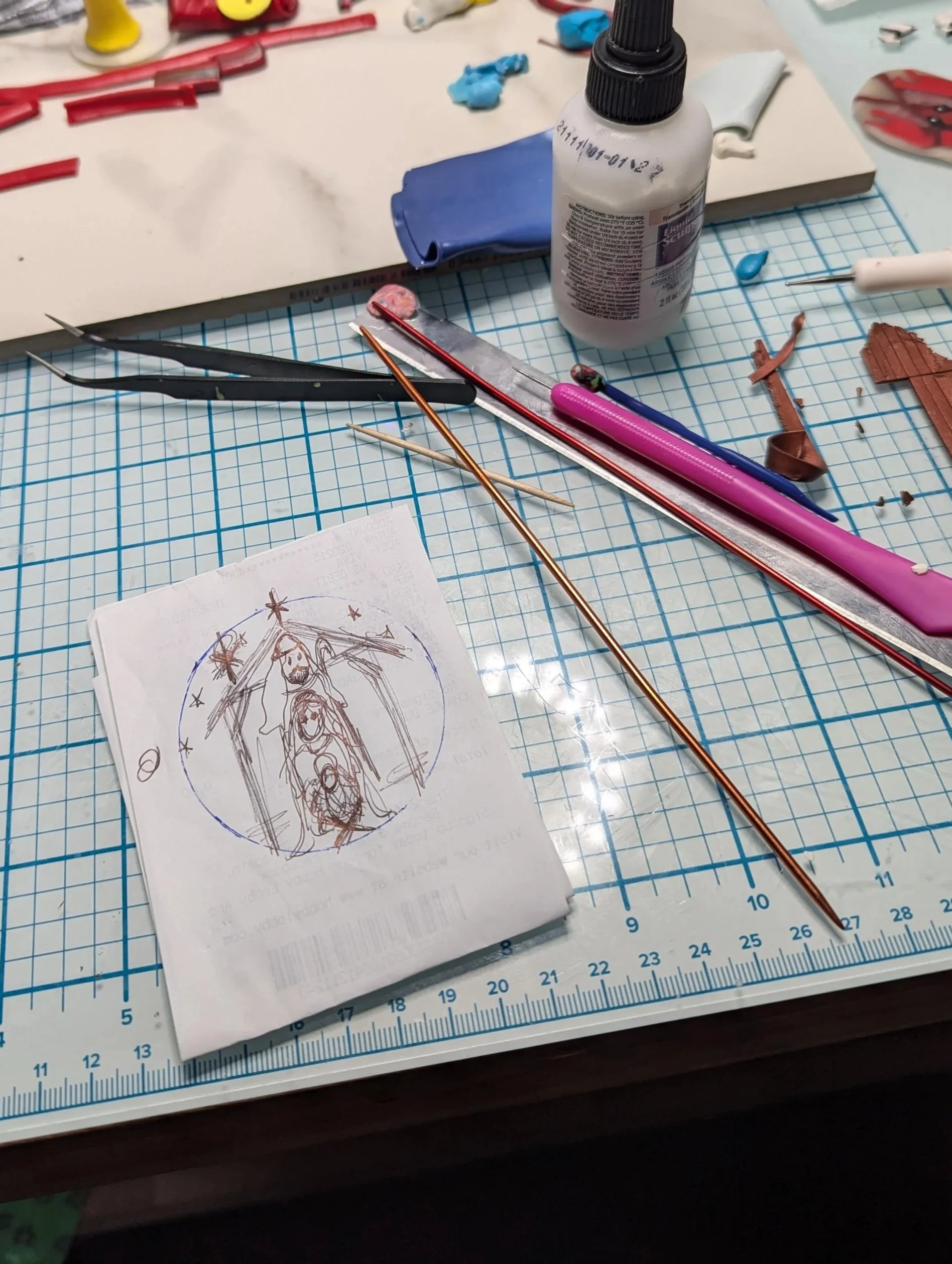 Studio process view of rough sketch-up of the Nativity Manger Ornaments by Art Illusions by Young. Tools and materials surround the hand-sculpted pieces in progress, showing the careful layering of polymer clay and texturing used to create the humble