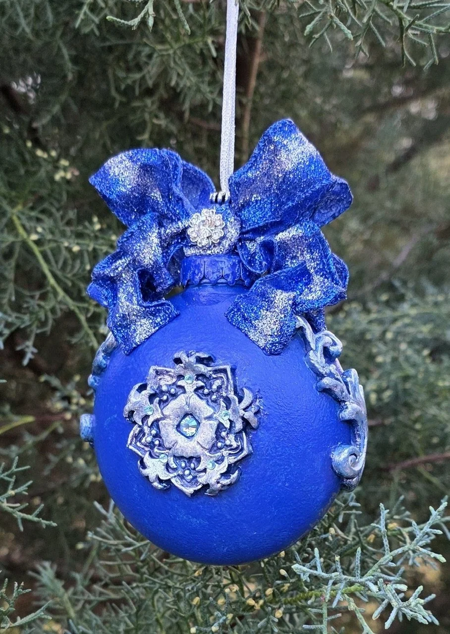 Angled rear view of the Celestial Blue Cross Ornament by Art Illusions by Young with ruler for scale. The hand-sculpted and molded cobalt blue orb showcases the ornate silver cross with filigree and scrollwork, crowned by a sparkling royal-blue and s