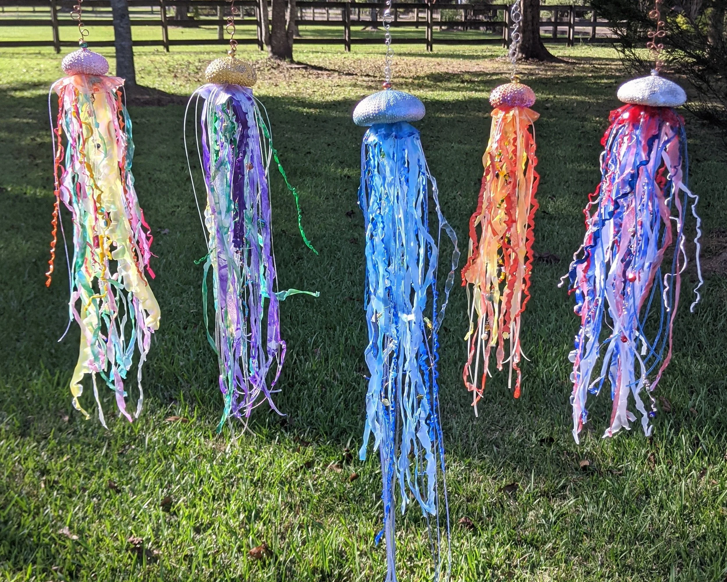 🔴 Sold: 
Jellyfish Suncatcher Collection Displayed Outdoors by Art Illusions by Young, Folsom, Louisiana. Five graceful jellyfish-inspired suncatchers hang in a garden setting, their long, flowing tentacles crafted from shimmering beads, and poly-sh