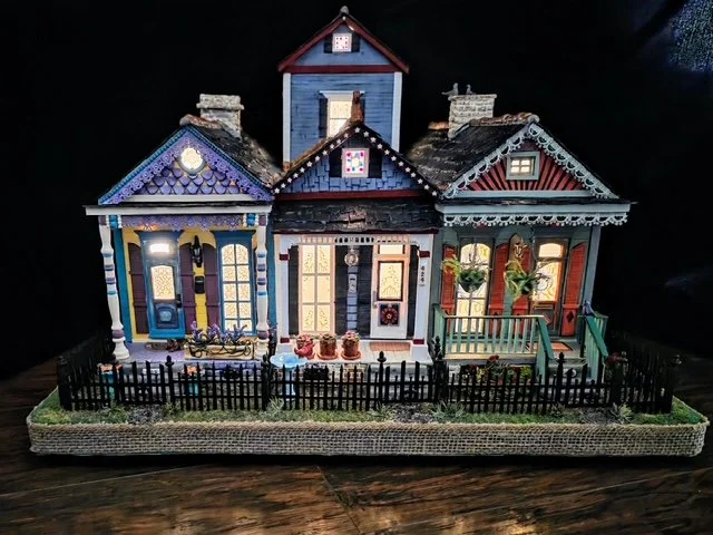 Frontal nighttime view of the handcrafted Triple New Orleans Shotgun House Row diorama by Art Illusions by Young. Illuminated from within, the three colorful shotgun houses glow with warm interior lighting that highlights intricate details: the sunny