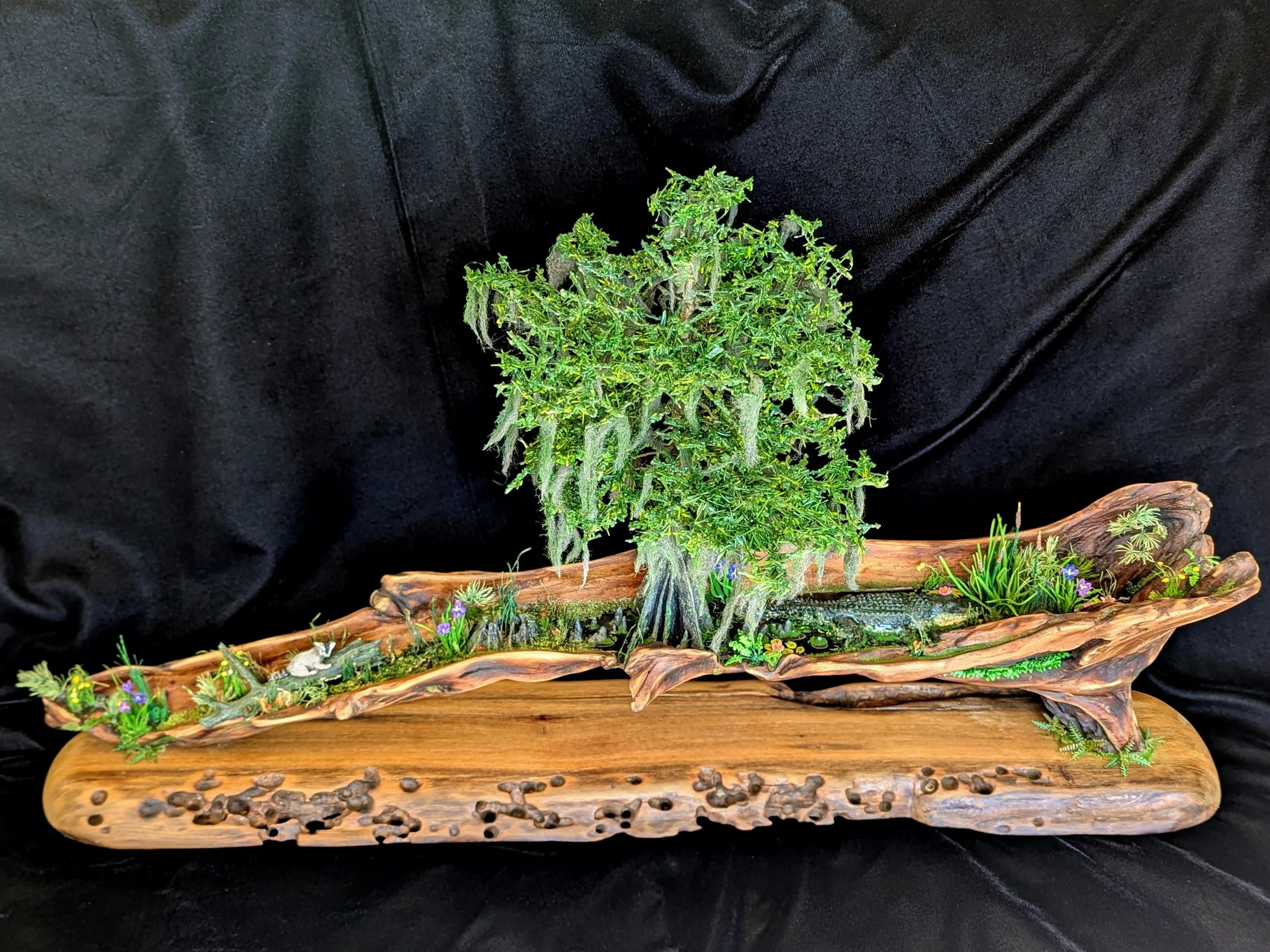 Handcrafted micro swamp and bonsai diorama by Art Illusions by Young in Folsom, Louisiana. A delicate miniature tree rises from a naturally curved sinker cypress driftwood base with realistic moss, grasses, and subtle epoxy water details. Part of the