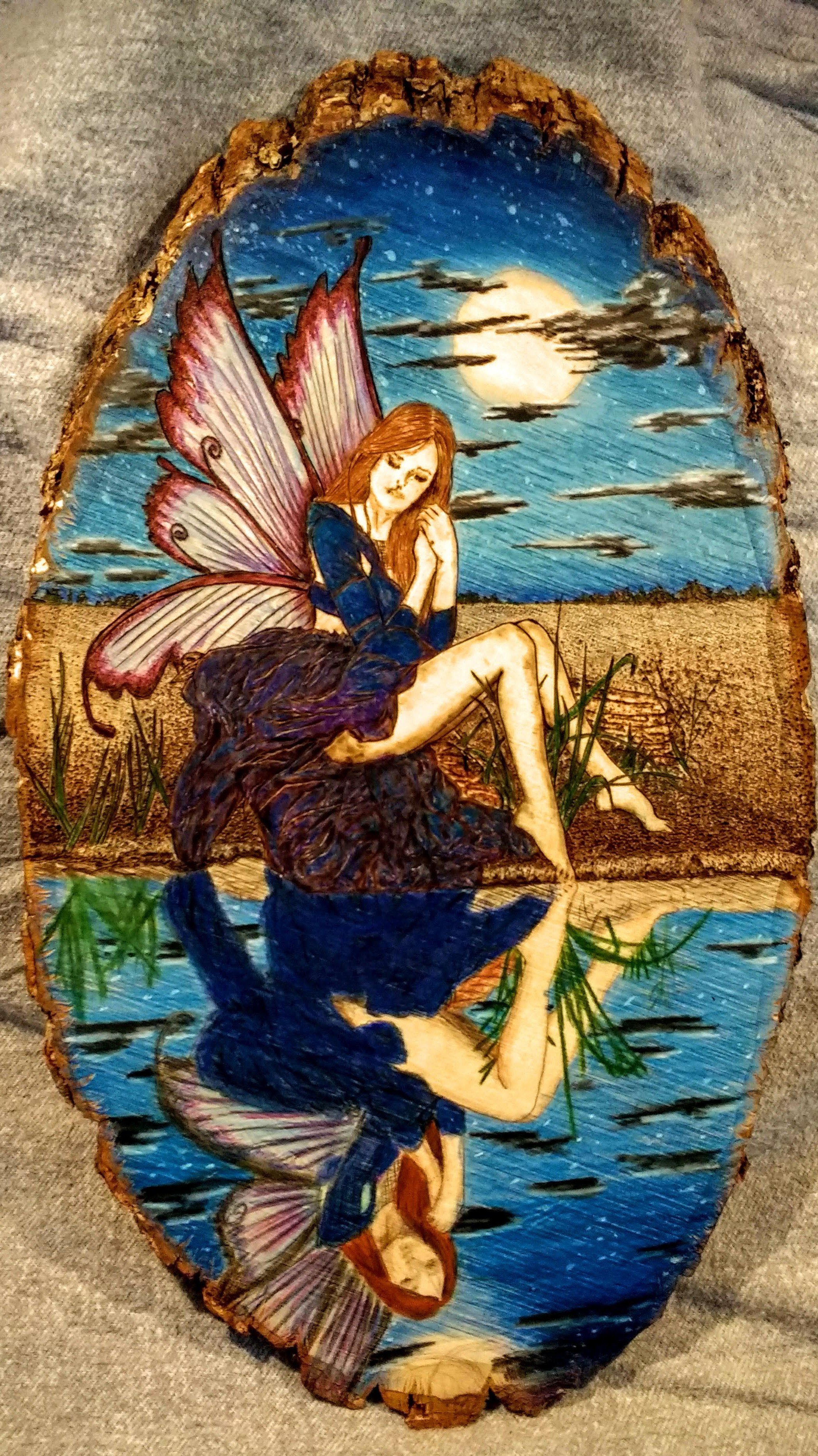 🔴 Sold:
Midnight Dreaming Pyrography by Art Illusions by Young, Folsom, Louisiana. This enchanting woodburn on a natural wood slice portrays a graceful fairy with iridescent wings seated beside a tranquil moonlit pond, her reflection perfectly mirro