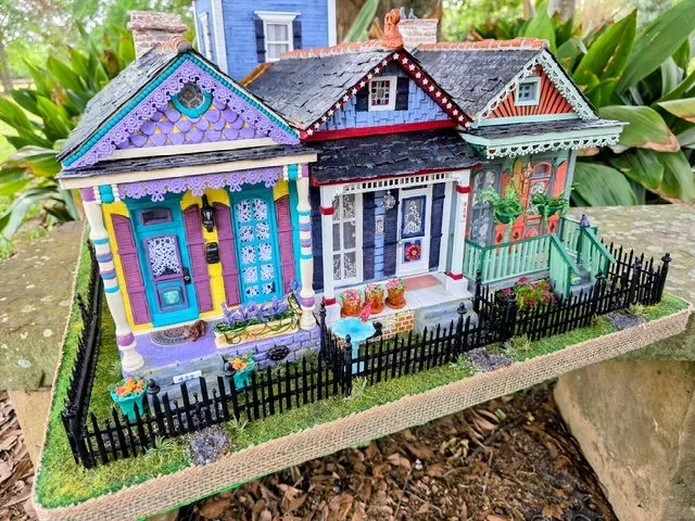 Angled front view of the handcrafted Triple New Orleans Shotgun Row diorama by Art Illusions by Young. This dynamic perspective beautifully displays all three colorful shotgun houses: the sunny yellow house with vibrant teal and purple accents on the