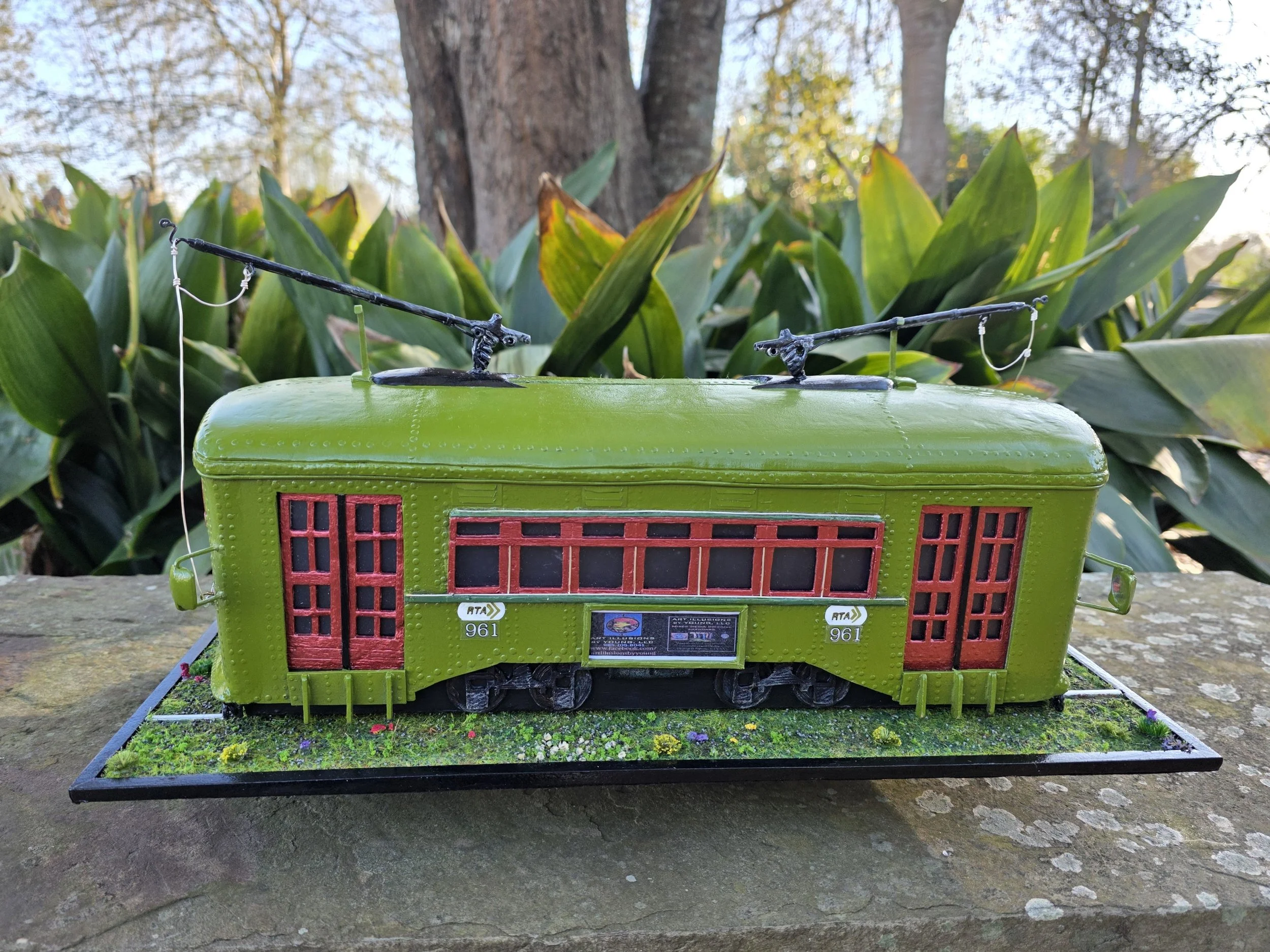 Rear side view of the olive green New Orleans streetcar artwork showing detailed windows, signage, and grassy base. Handcrafted mixed media functional art piece by Art Illusions by Young.