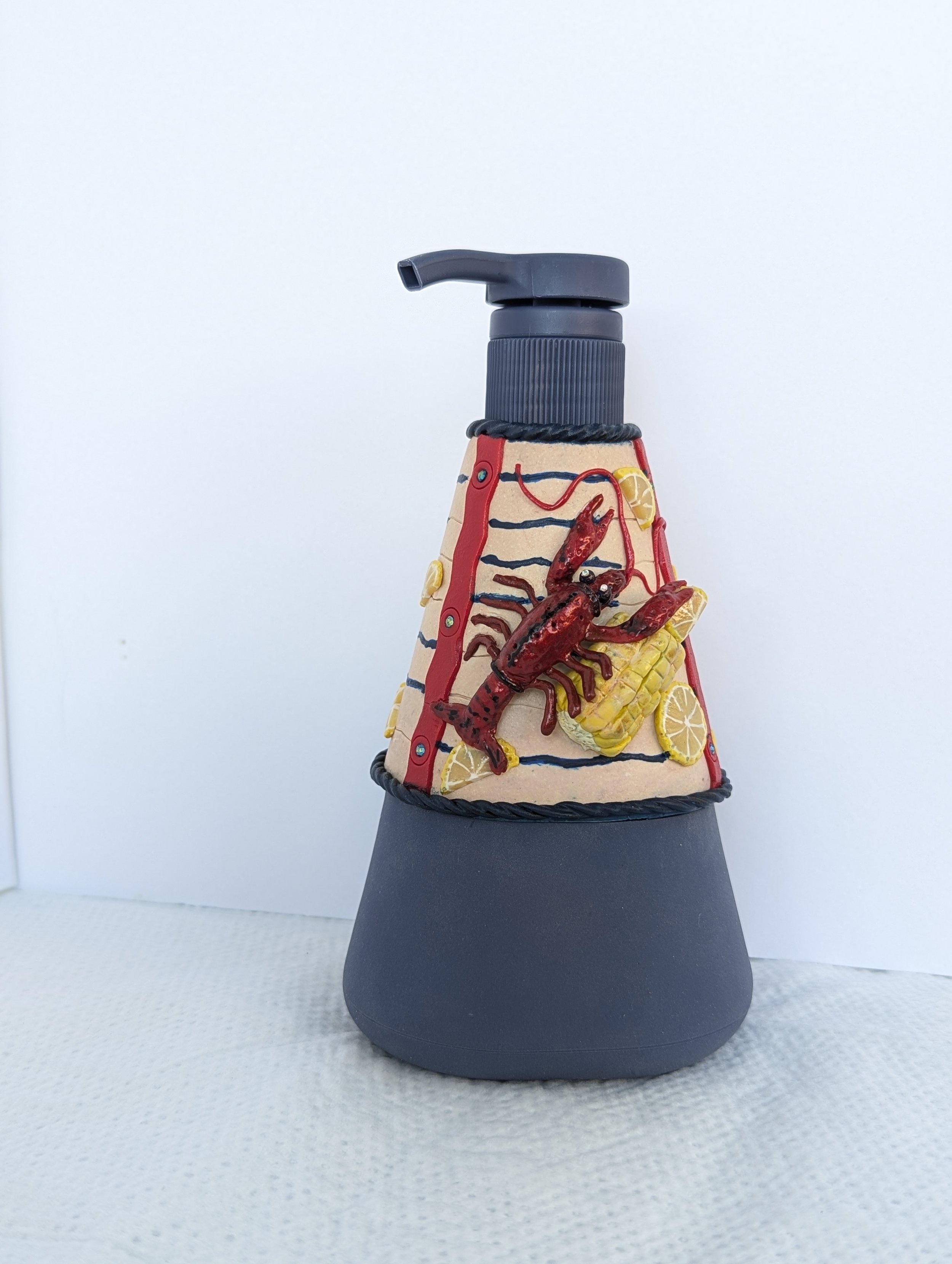 Crawfish Boil Soap Dispenser by Art Illusions by Young from Folsom, Louisiana. This functional work of art features a triangular silicone-bottomed glass bottle with our polymer clay artwork, meticulously hand-sculpted with bright red crawfish, golden