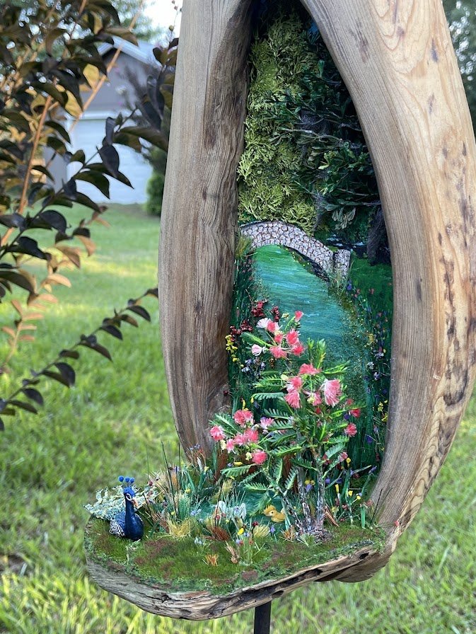 Side view of the Enchanted City Park Serenity micro diorama featuring the cypress hollow tree trunk, serene epoxy pond, and detailed landscaping with flowers and foliage. Handcrafted by Art Illusions by Young.