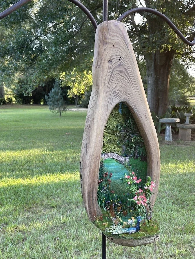 Handcrafted Enchanted City Park Serenity diorama by Art Illusions by Young in Folsom, Louisiana. A large hollowed sinker cypress tree trunk reveals a miniature park scene with reflective epoxy pond, arched bridge, pink flowers, and lush landscaping, 