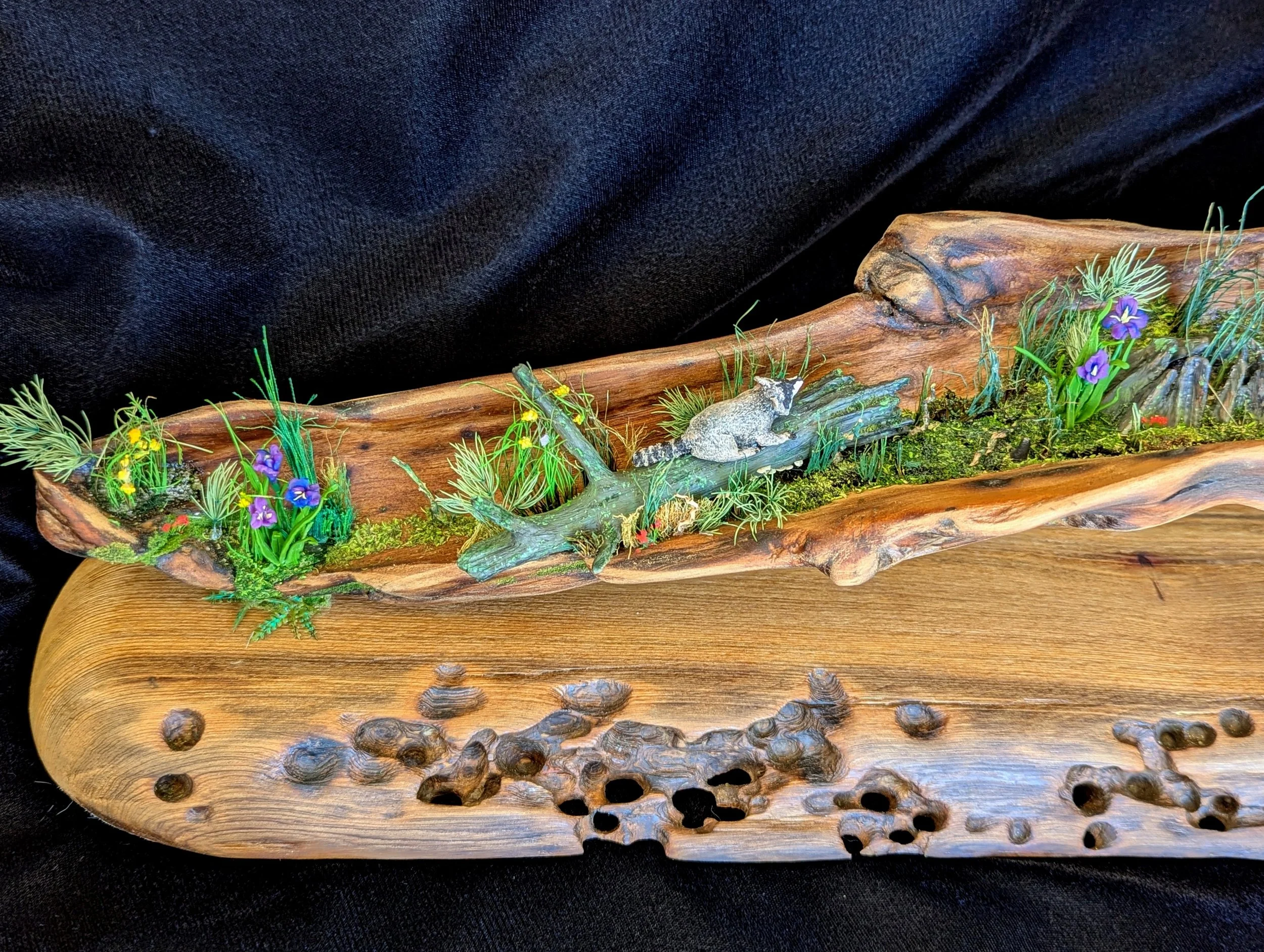 Side profile of a handcrafted micro swamp landscape on driftwood base with purple irises, yellow wildflowers, moss, and textured soil layers. Detailed mixed media work by Art Illusions by Young in Folsom, Louisiana.