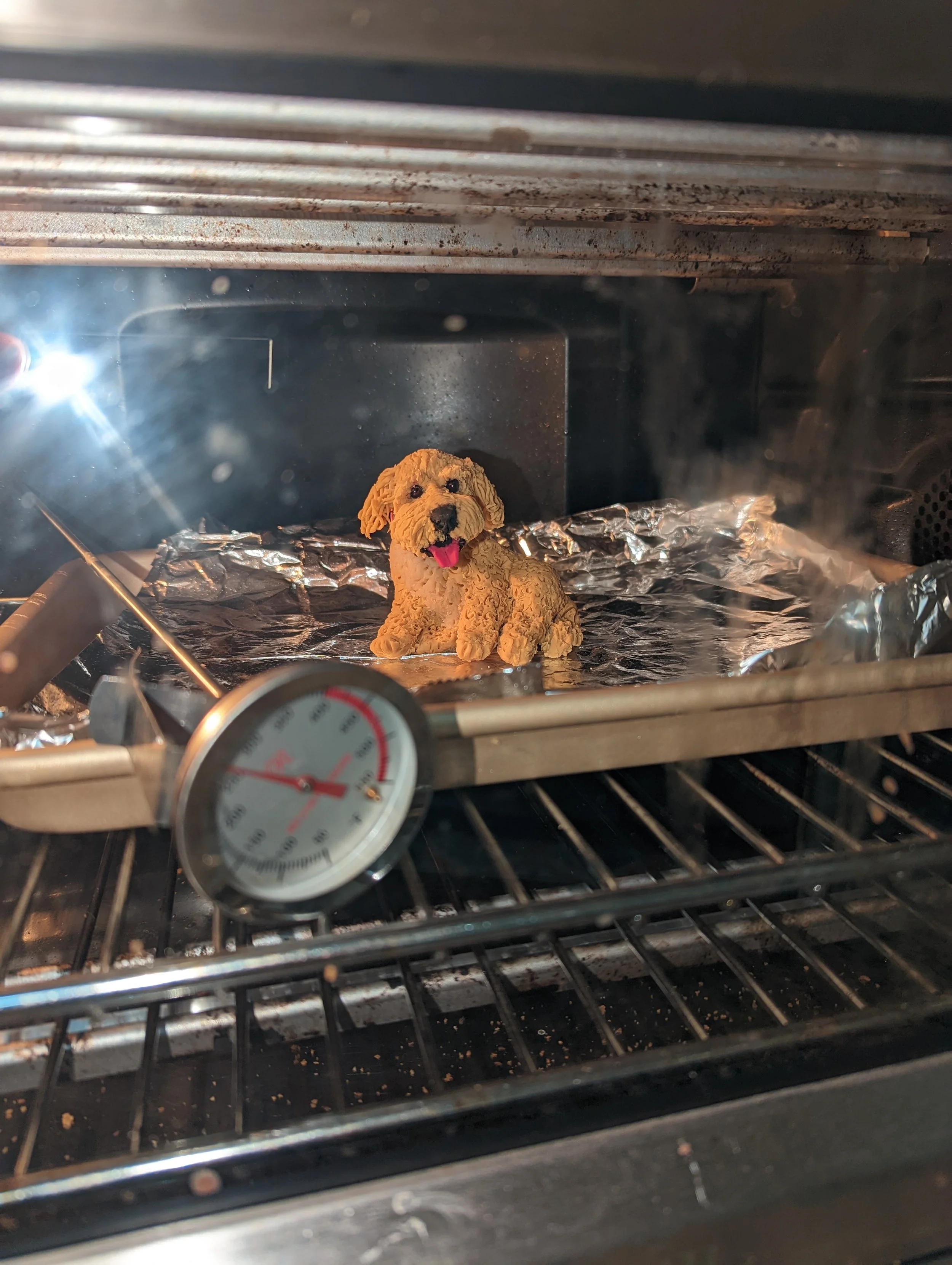 Studio process shot of the Puppy Commission Mobile by Art Illusions by Young. The hand-sculpted polymer clay likeness of the family dog “Puppy” is shown curing in the oven, capturing one of the many careful steps required to create this personalized 