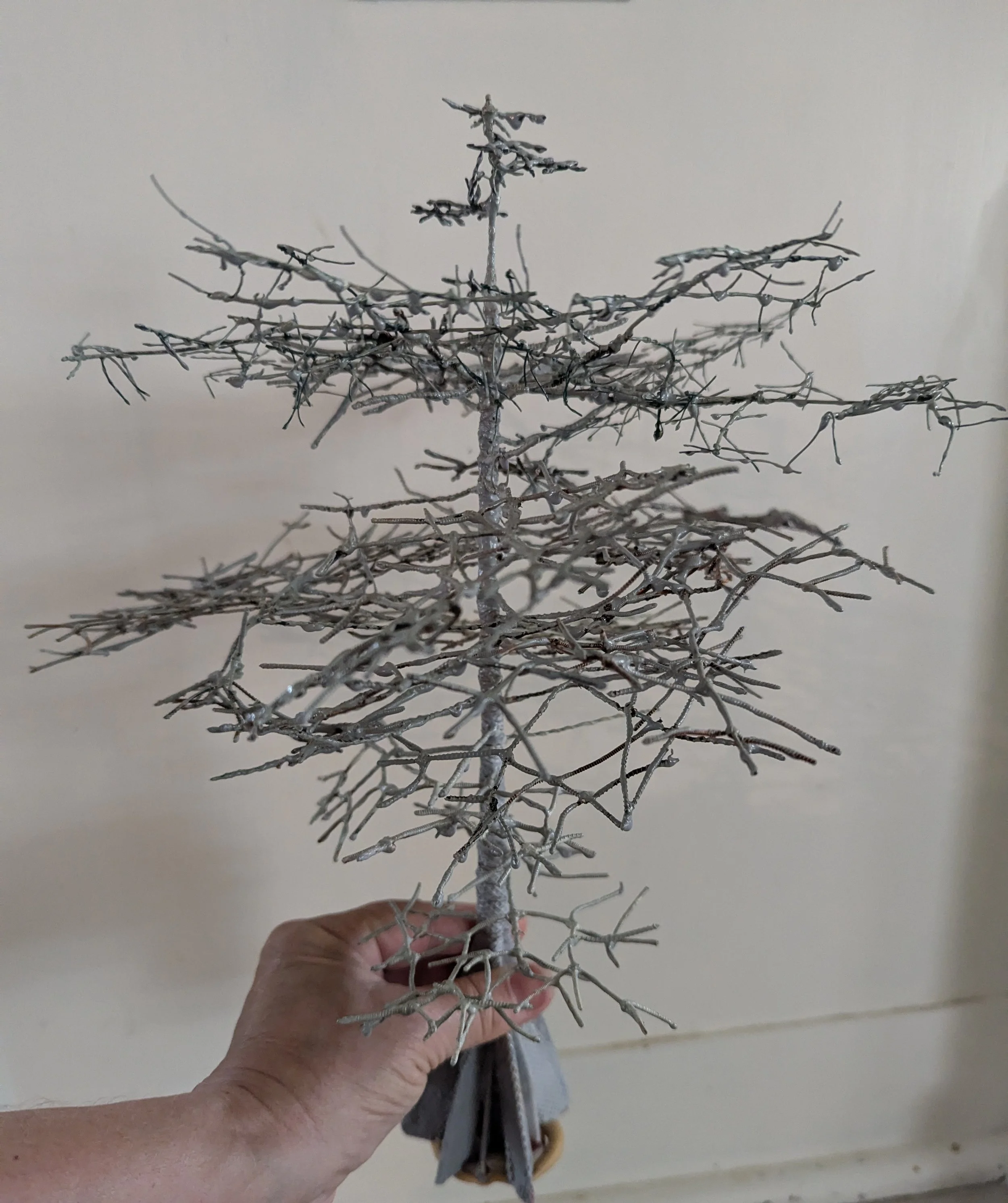Bare miniature tree framework hand-woven from copper wire, forming the structural skeleton for a micro swamp bonsai diorama by Art Illusions by Young. Early sculpting stage showing intricate branching before foliage and moss are added.