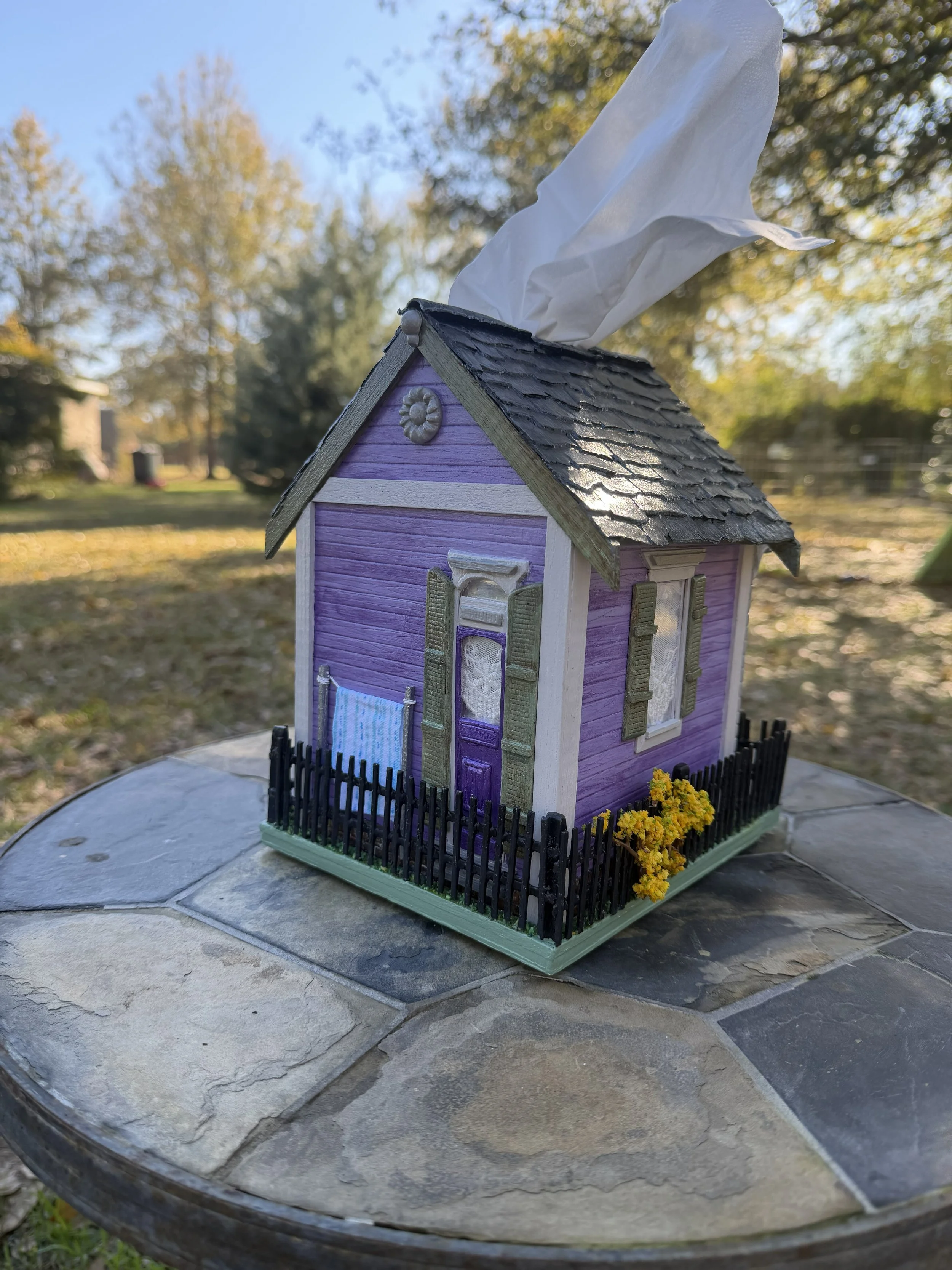 Side and rear profile of the Purple Reign Shotgun House tissue box cover diorama by Art Illusions by Young. Shows transoms, corbels, quions, sage green shutters, and the full black wooden "wrought iron" fence enclosing the miniature yard. Meticulousl