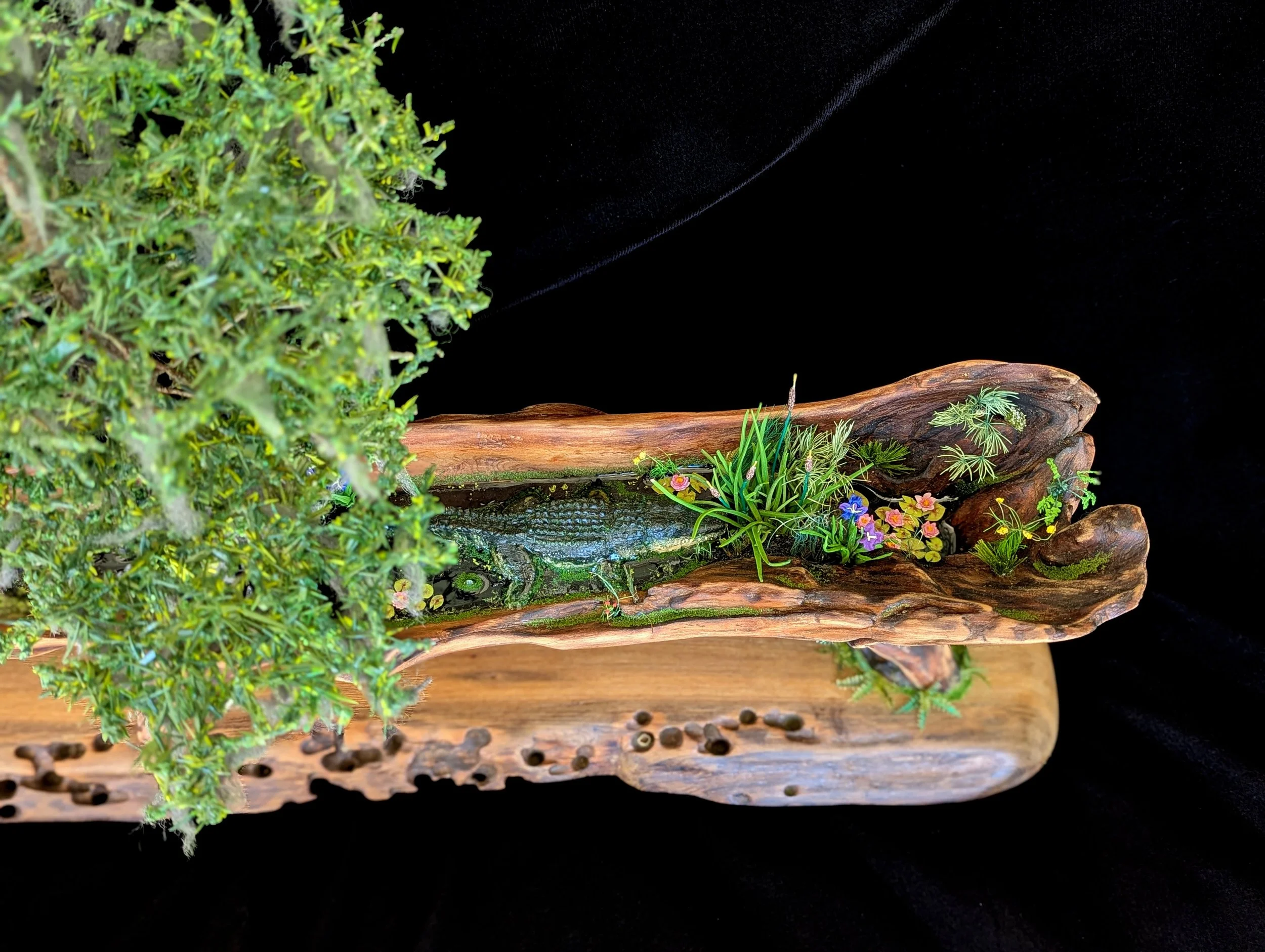 Close-up detail of hand-sculpted moss, grasses, and polymer clay foliage on a weathered driftwood base in a micro swamp diorama by Art Illusions by Young. Realistic textures and natural elements create an intimate Louisiana wetland scene.